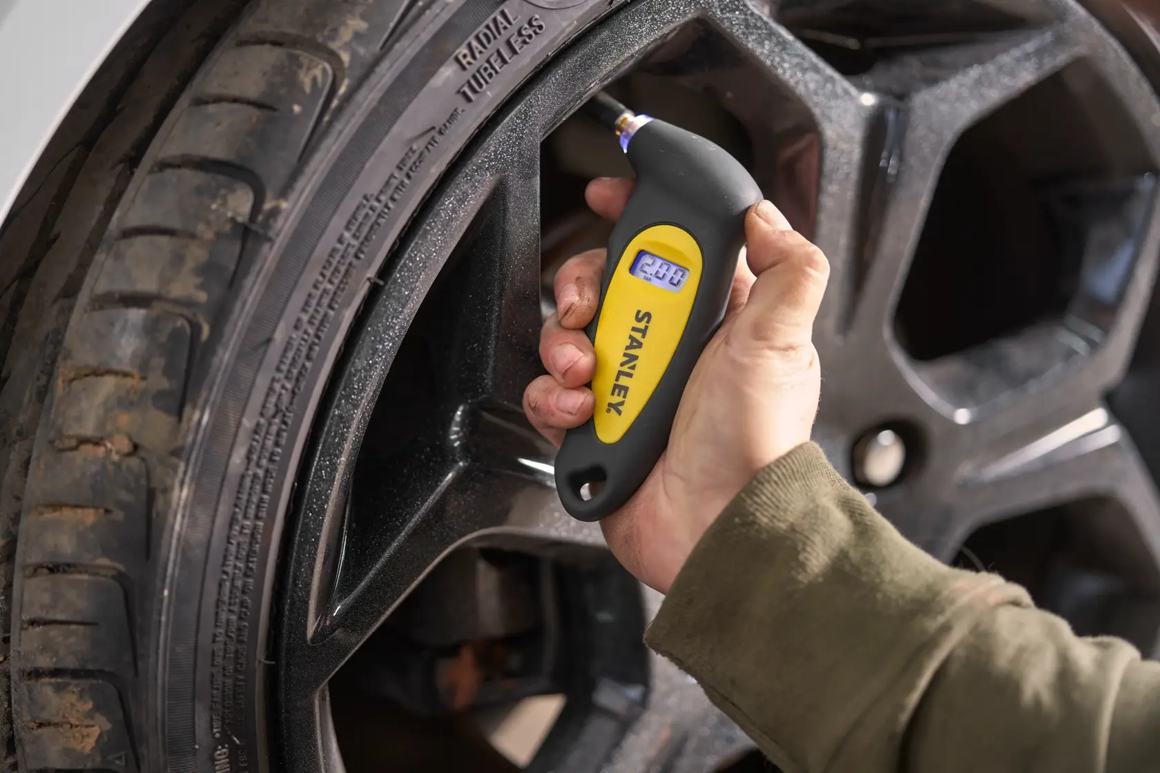 STANLEY STHT80874-0 digital tire pressure gauge checking car tire, close-up photography.
