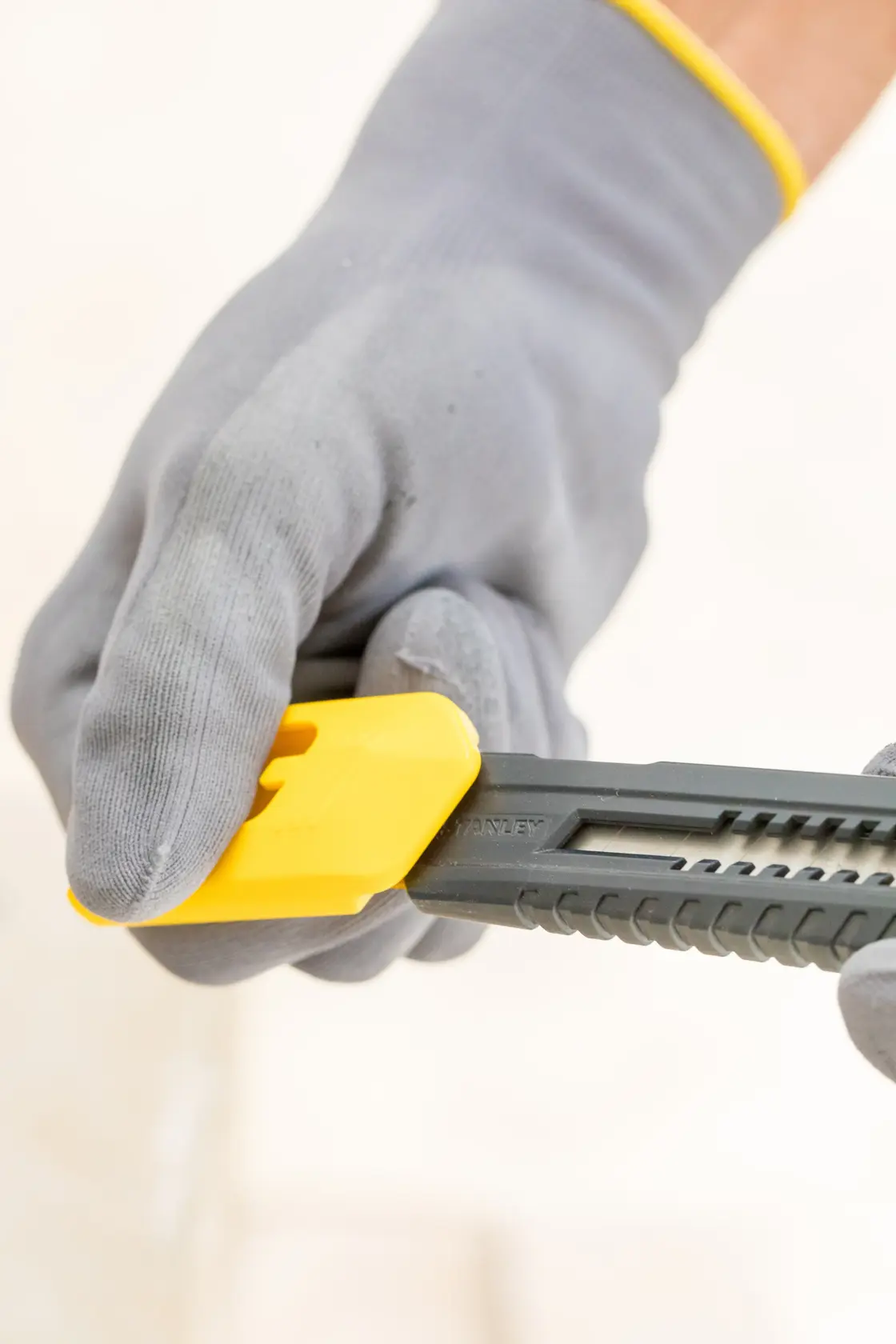 STANLEY 0-10-151 utility knife with yellow slider held by gloved hand, close-up side view.