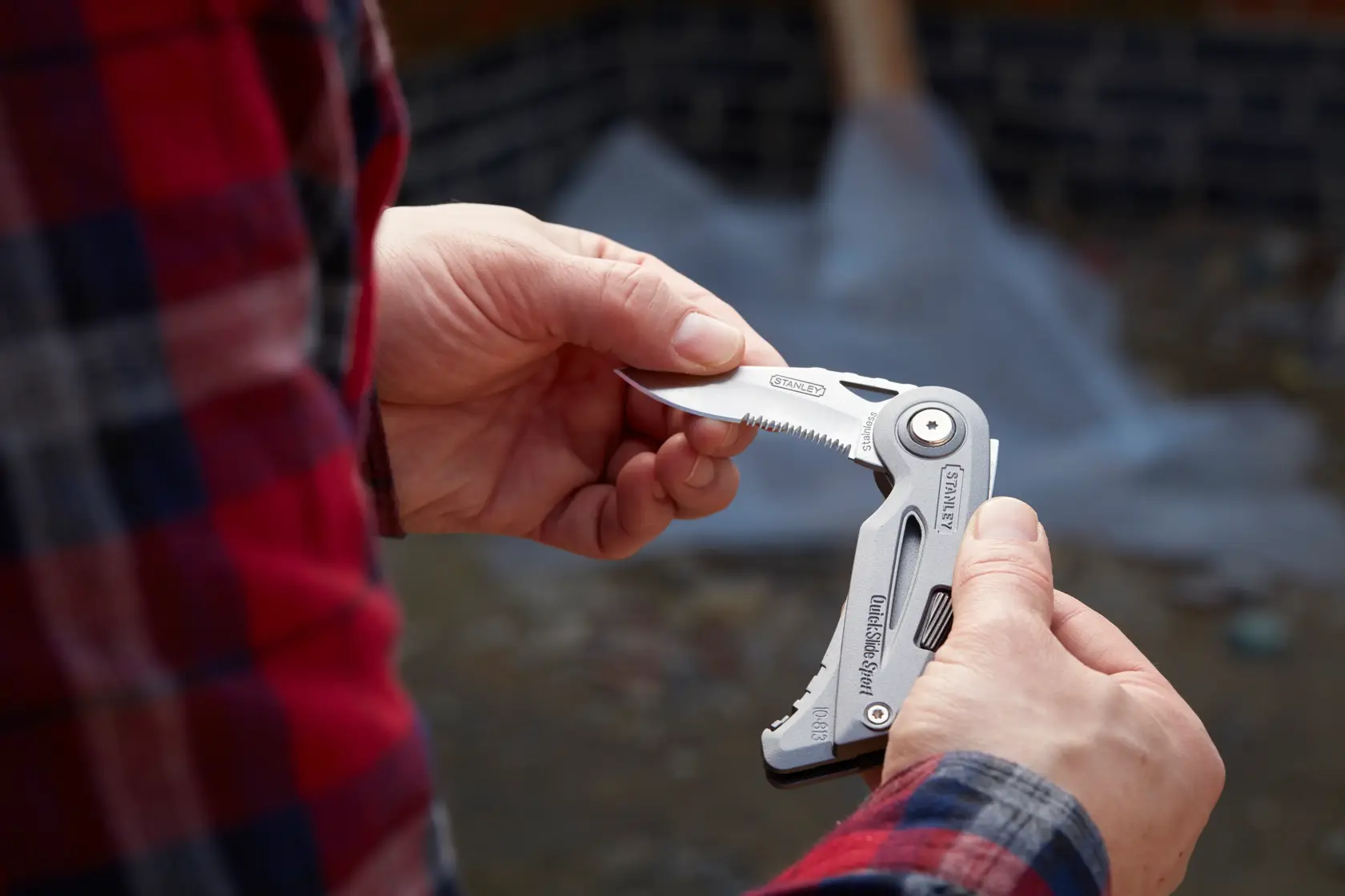 Photo of STANLEY 0-10-813 multitool knife being held outdoors, partially open showing serrated blade.