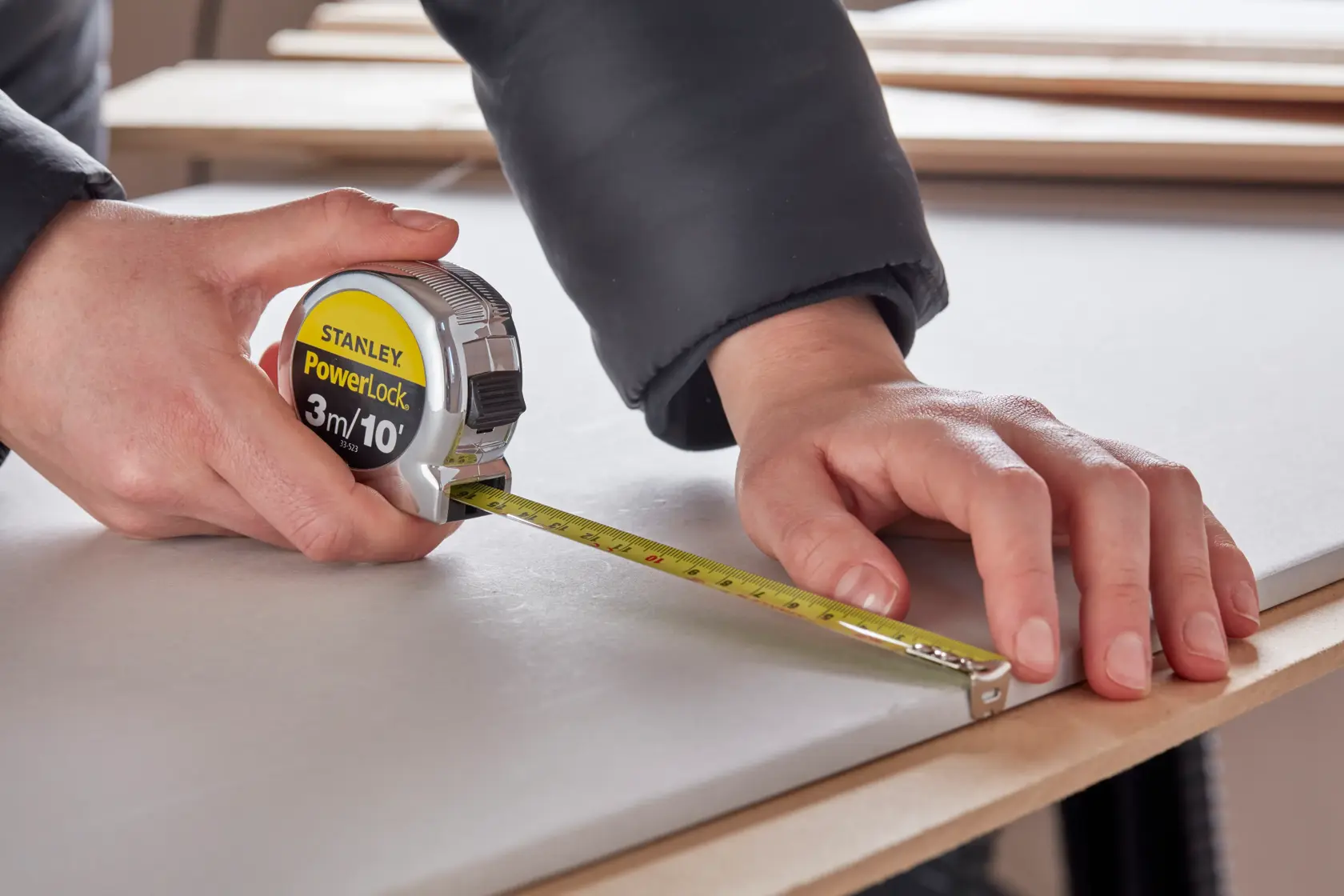 Photo of STANLEY 0-33-523 tape measure in use on a work surface, measuring wood, close-up angle.