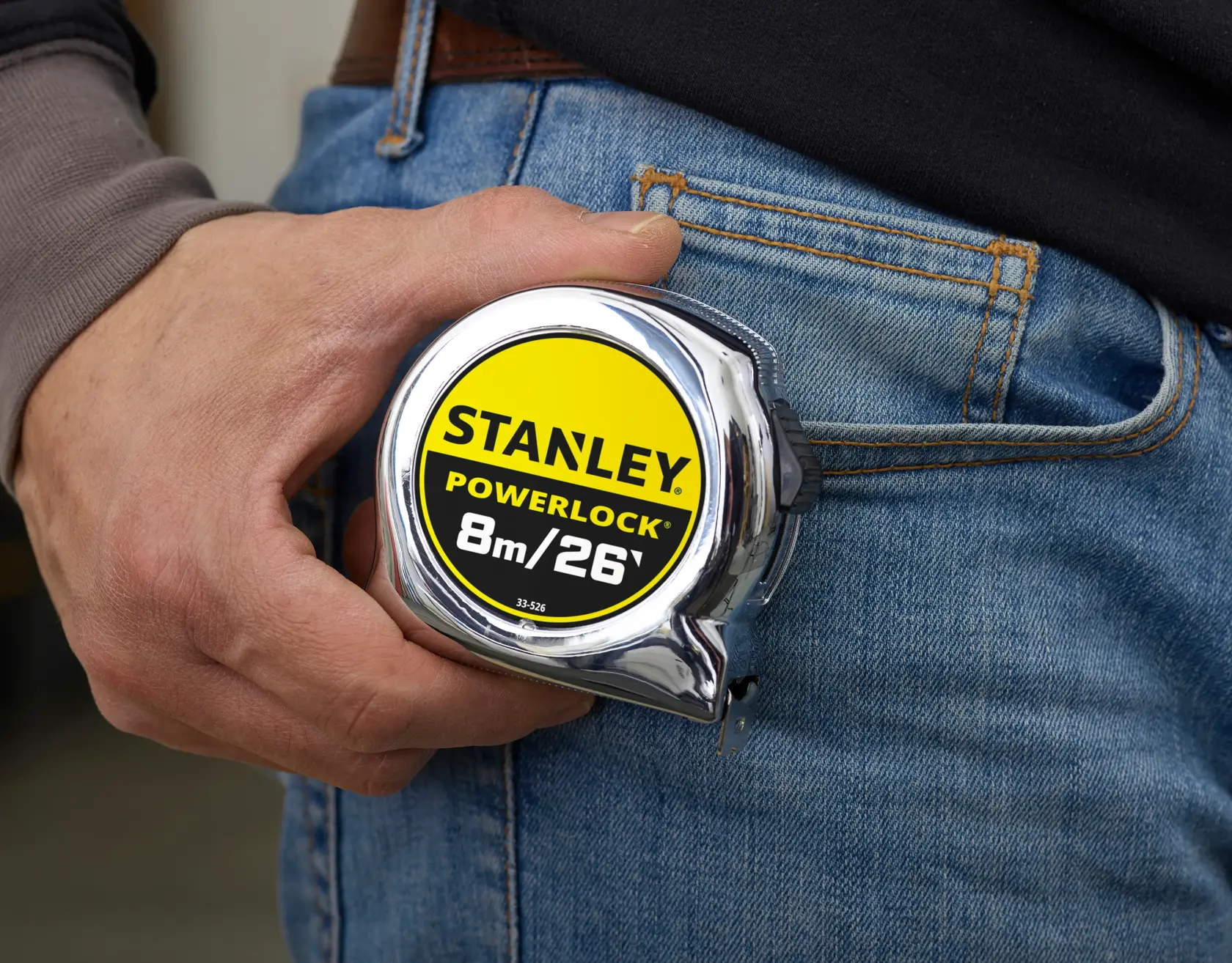 STANLEY 0-33-526 tape measure PowerLock BladeArmor 8m/26ft held in hand next to jeans.