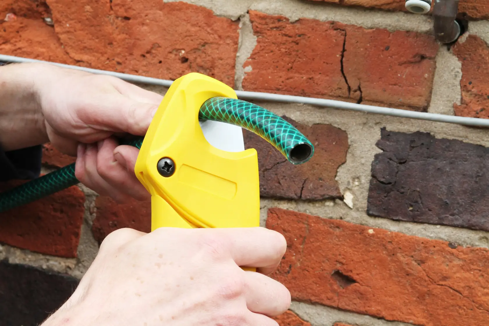 Photo of STANLEY 0-70-450 hose cutter cutting green garden hose against brick wall.