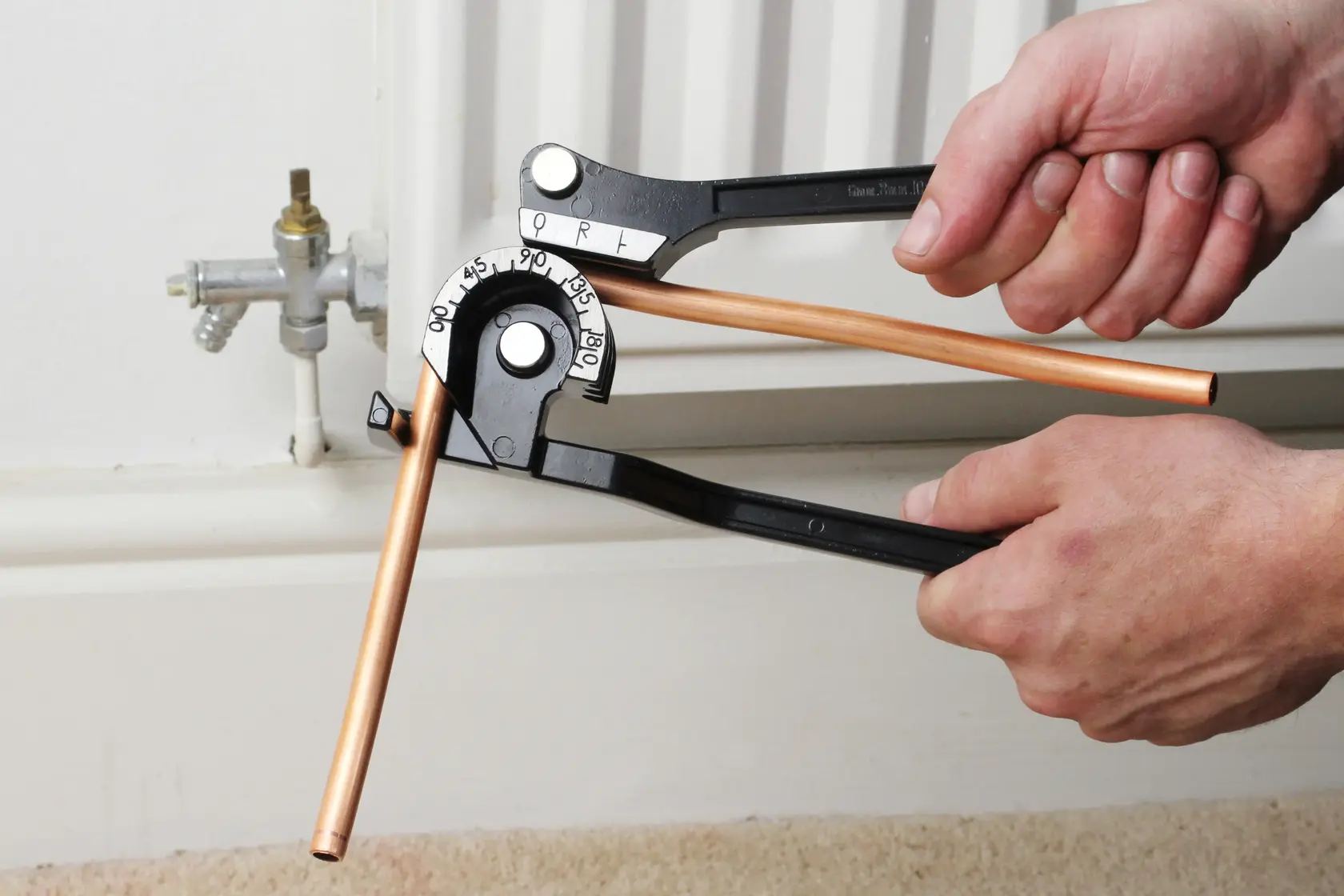 STANLEY 0-70-451 pipe bender bending copper pipe near radiator, close-up in use.