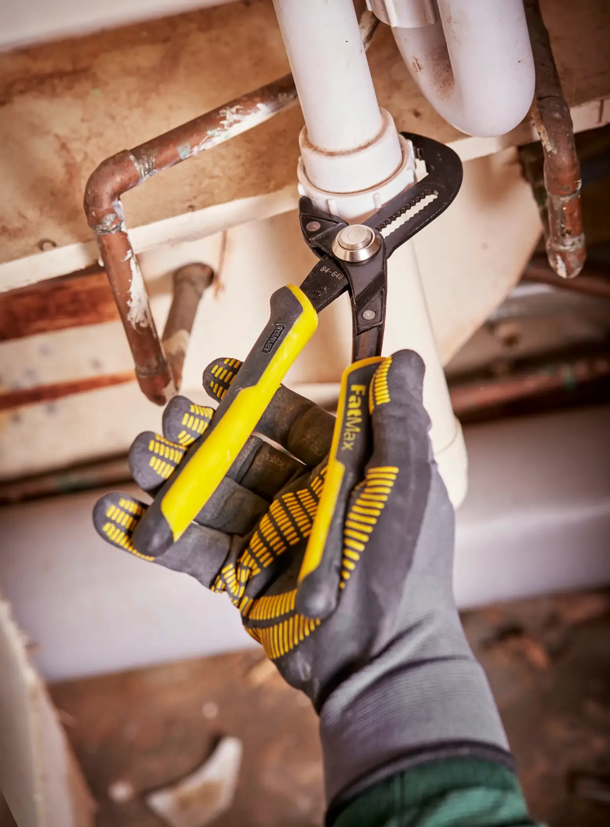STANLEY 0-84-648 pliers with yellow handles used for plumbing under sink, close-up photography.