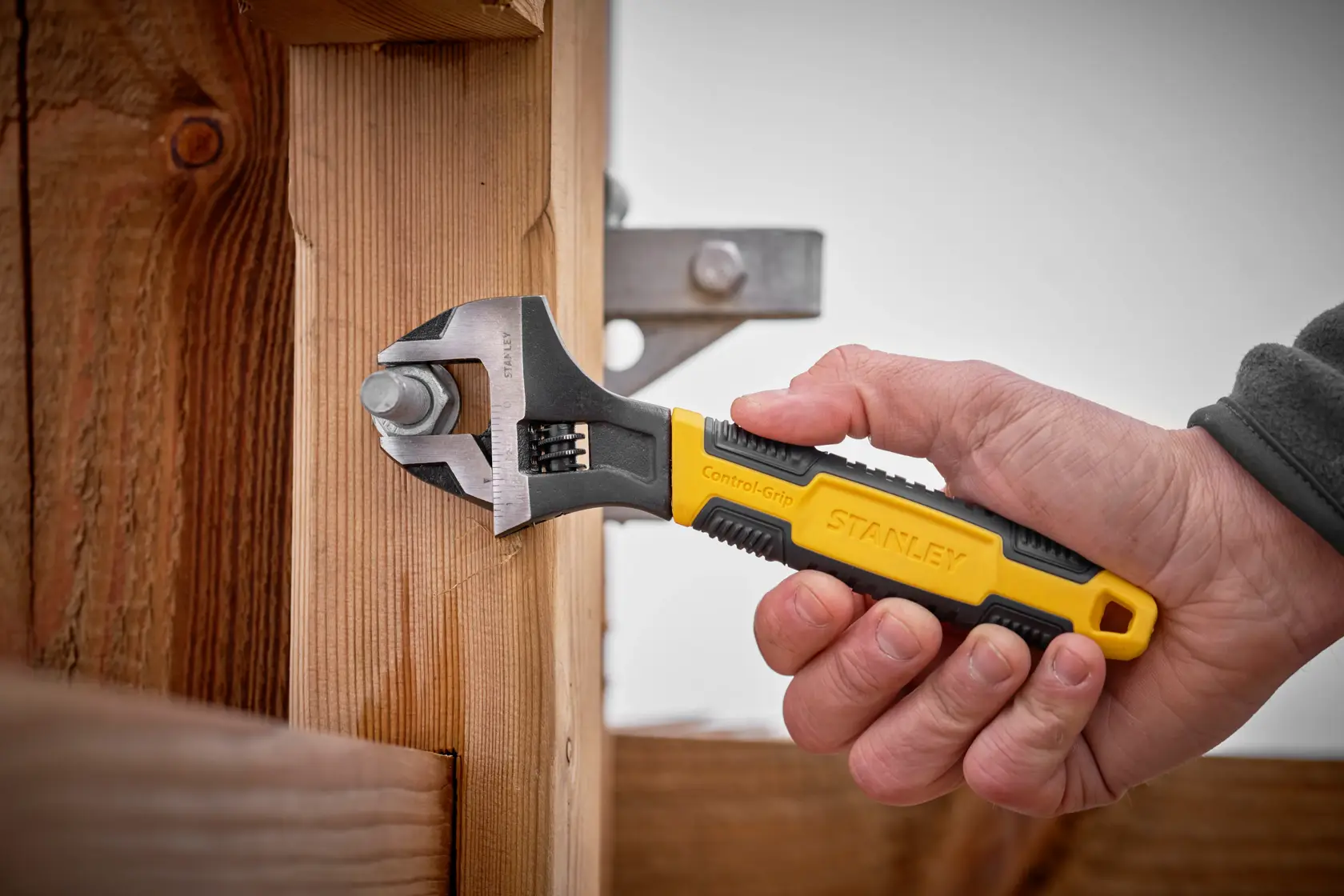 STANLEY 0-90-950 adjustable wrench with yellow and black handle tightening bolt on wooden post.