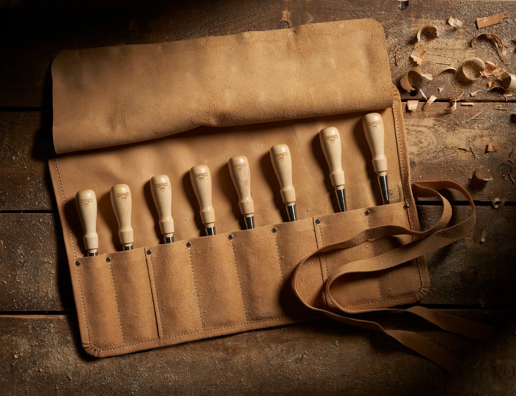 STANLEY 1-16-793 chisel set in tan suede roll, wooden handles, photographed from above on rustic table.