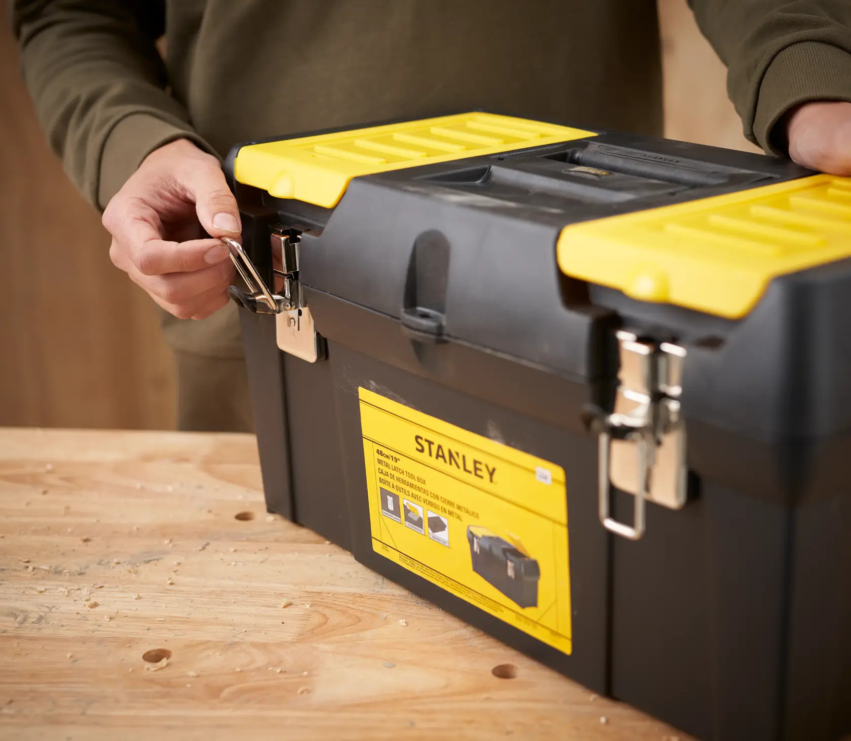STANLEY 1-92-066 tool box with yellow lid and metal latches, front angle, on wooden table.