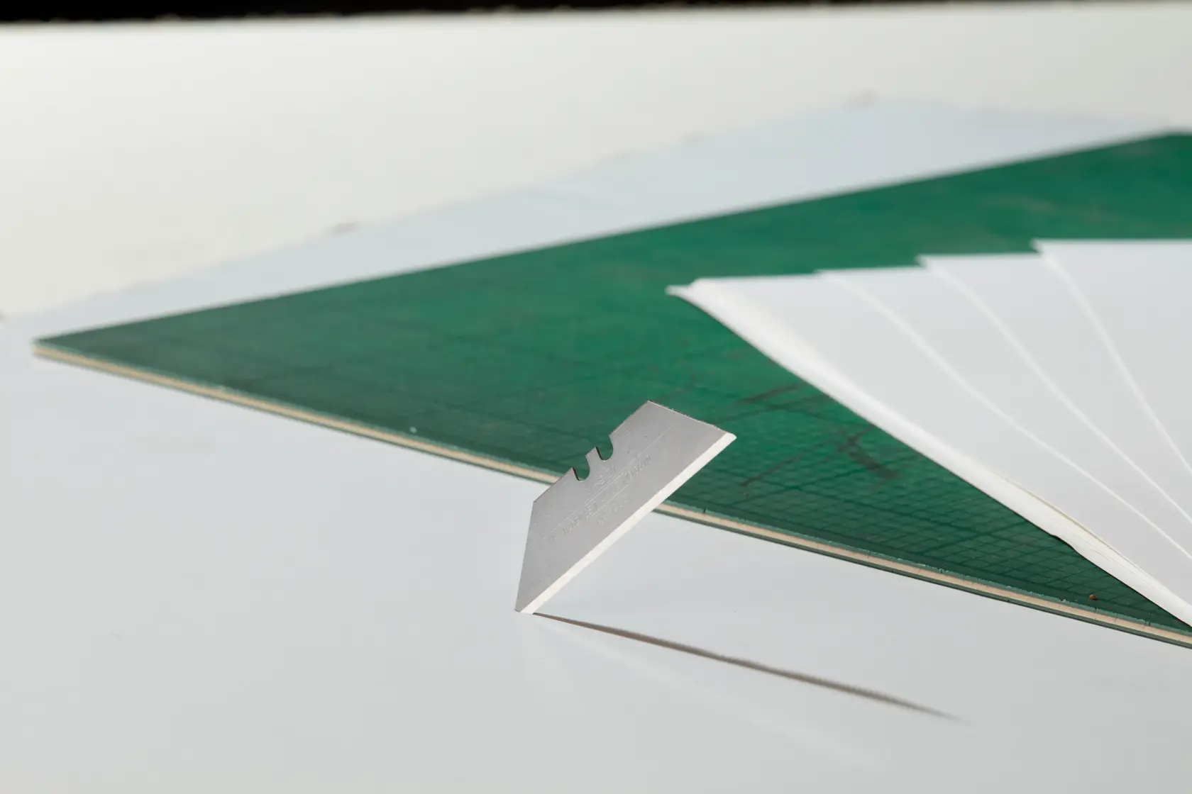 STANLEY 1-98-460 razor blade upright on green cutting mat with sheets, side angle, photography product.