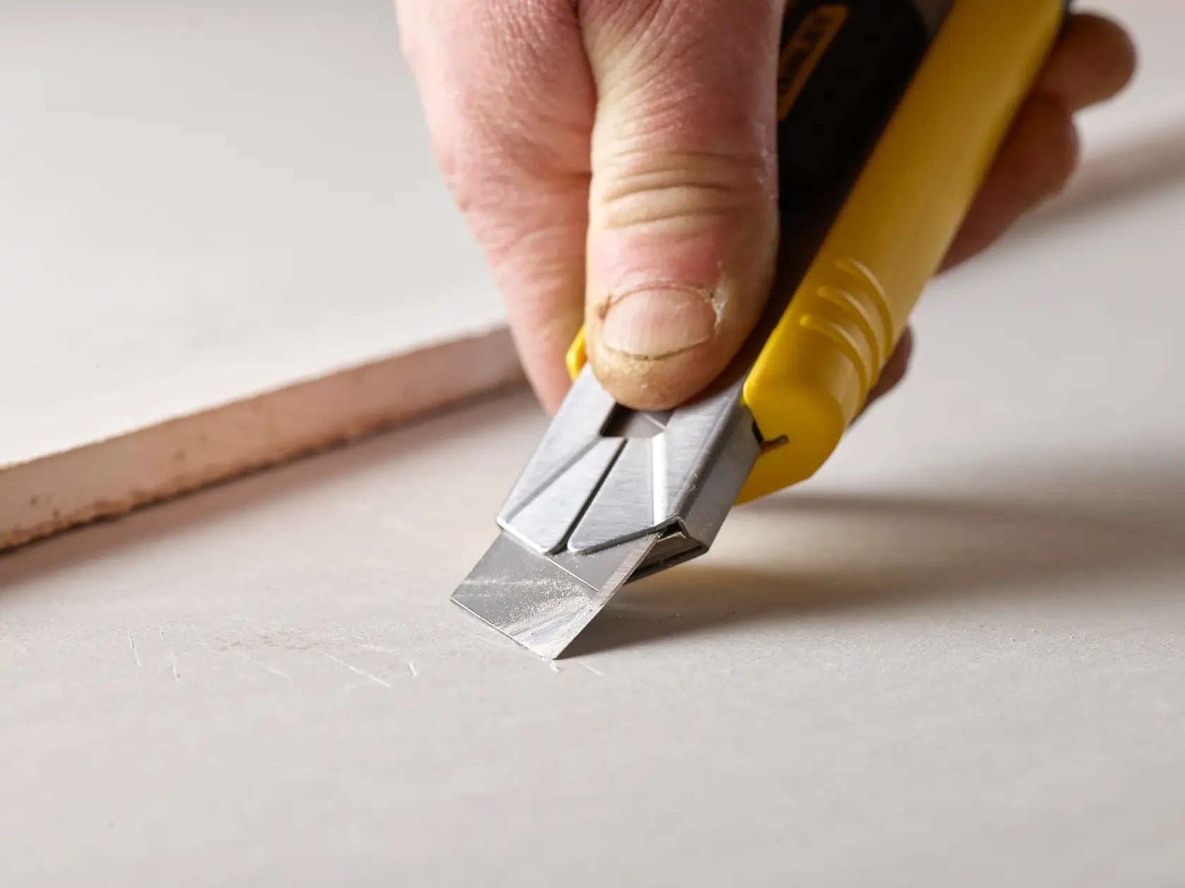 Photo of STANLEY 2-11-725 utility knife cutting drywall sheet close-up, showing yellow handle and metal blade.