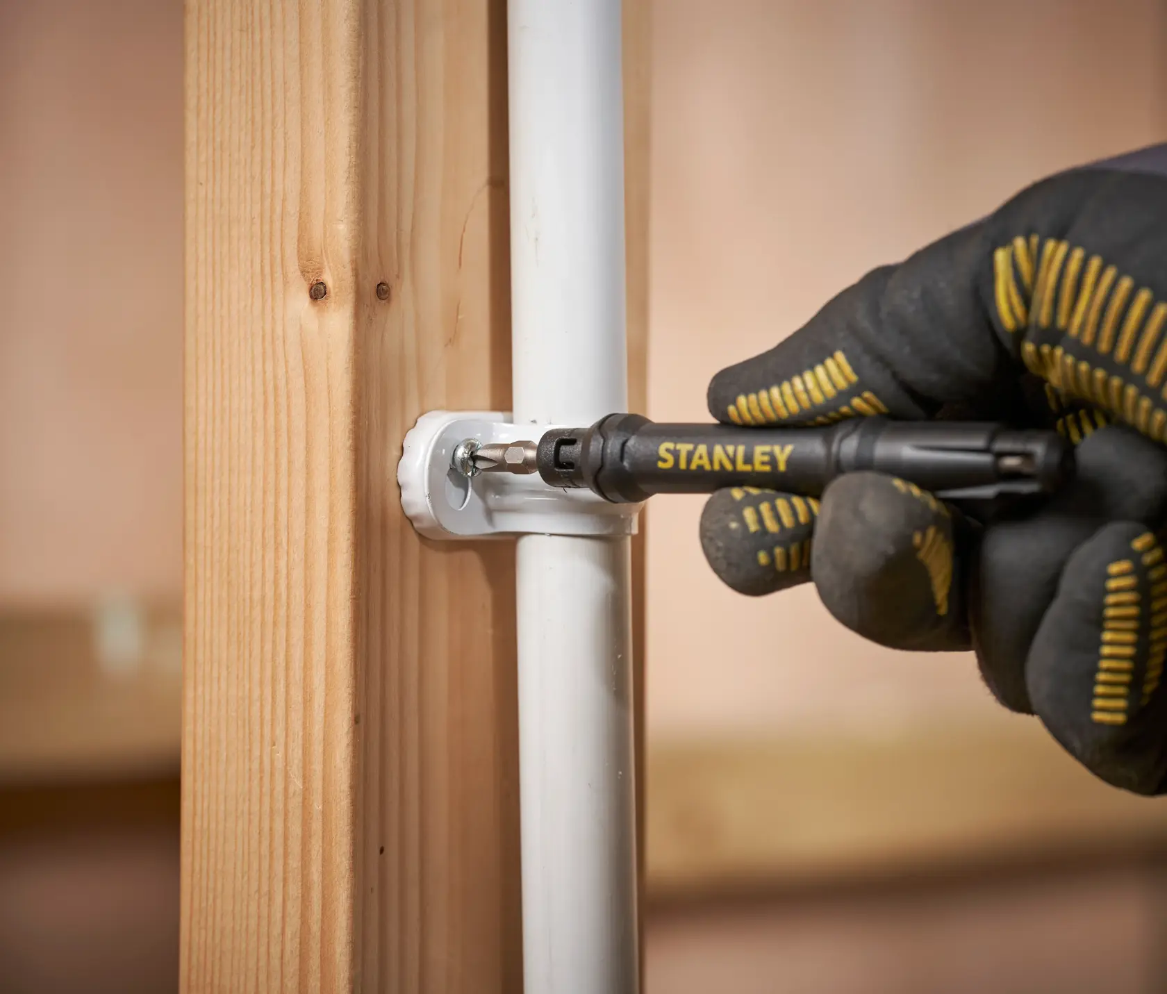 Photo of STANLEY 66-344M screwdriver securing pipe bracket to wooden post, close-up view.