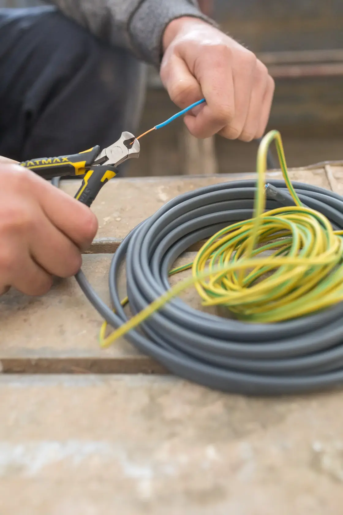 STANLEY FMHT0-80541 diagonal pliers cutting electrical wire, with coiled cables on a workbench.
