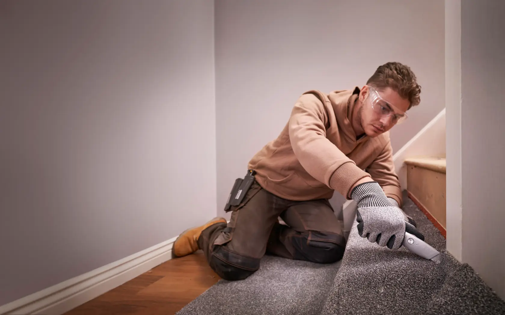 STANLEY FMHT10501-0 utility knife cutting carpet on stairs, shown in use by worker wearing gloves.