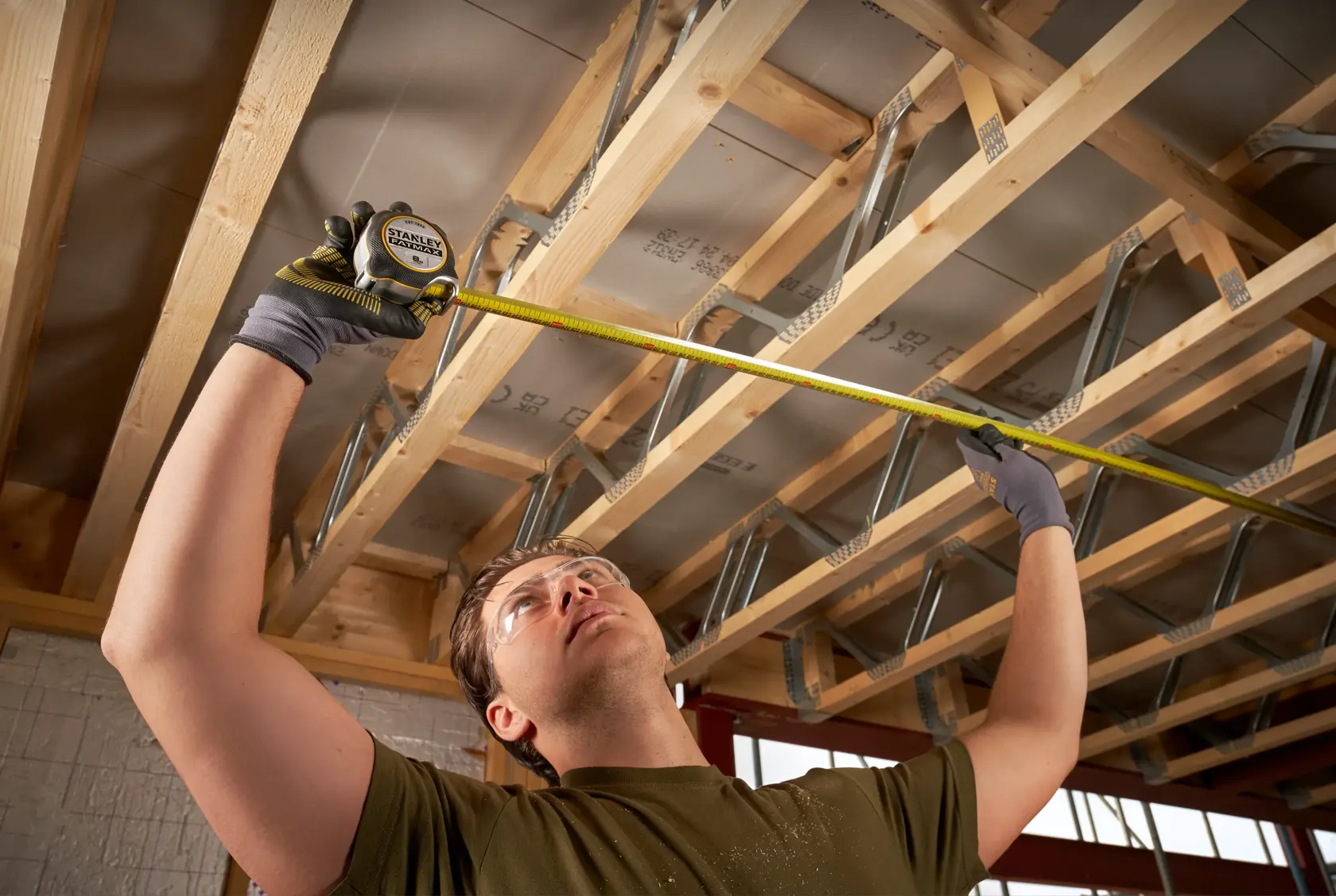 STANLEY FMHT38217-0 tape measure used by person measuring wooden ceiling beams on construction site.