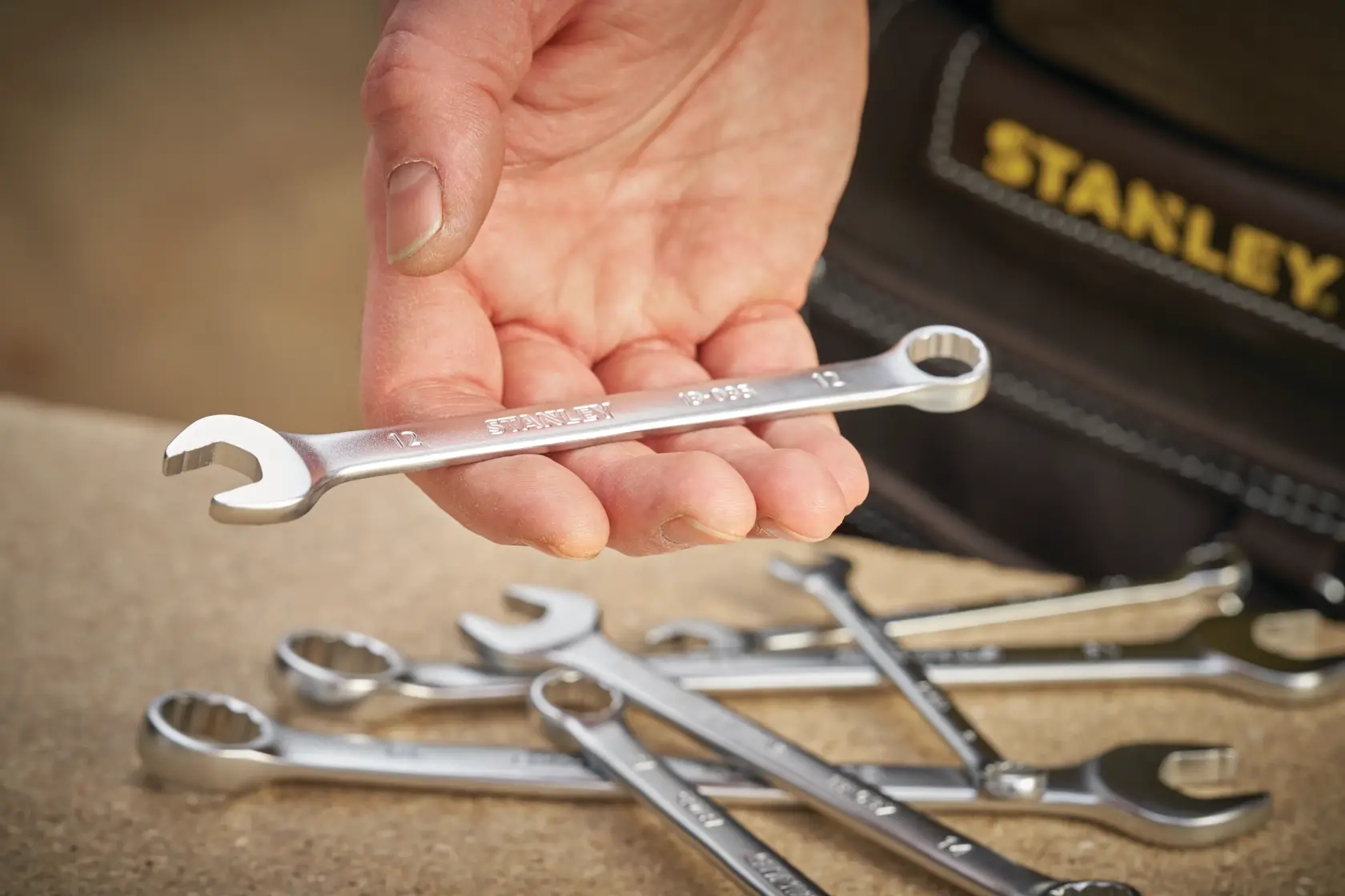 STANLEY FMMT13033-0 combination wrench held in hand, several wrenches on workbench, close-up photography.