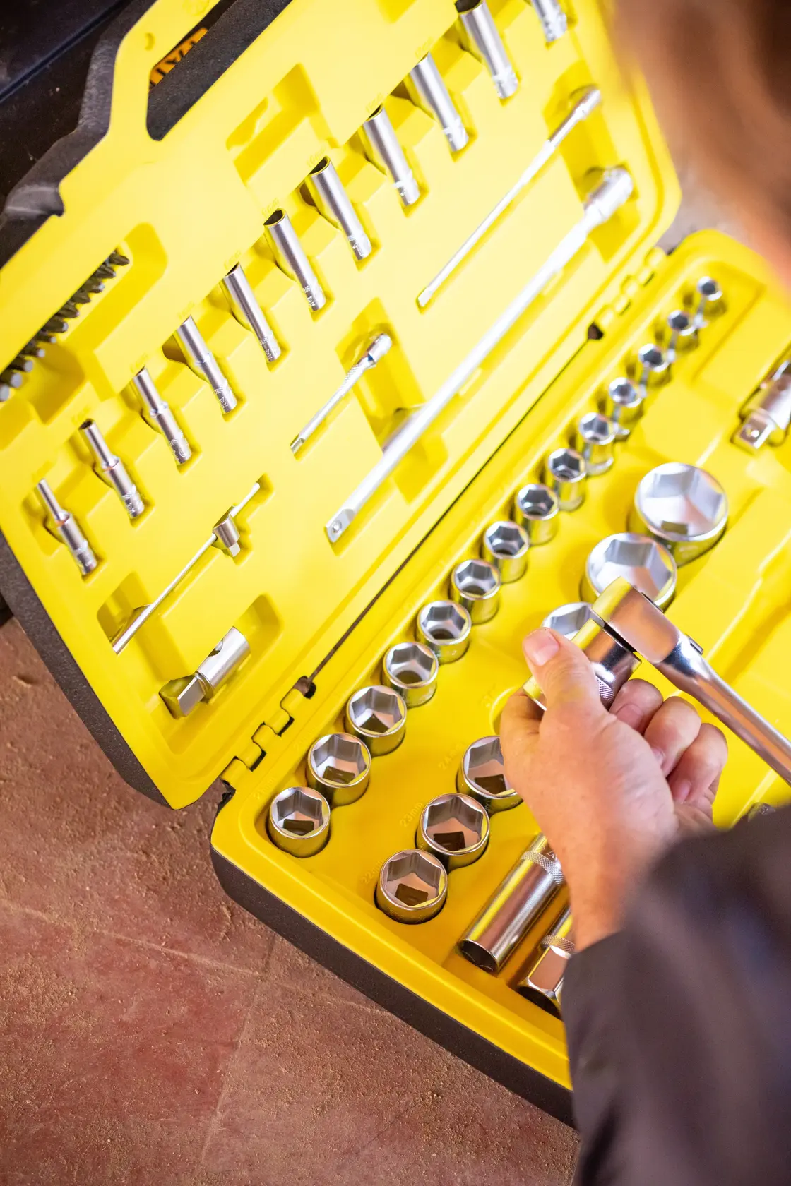 STANLEY FMMT82685-1 socket set with ratchet and sockets in yellow case, hand holding a tool, top view.