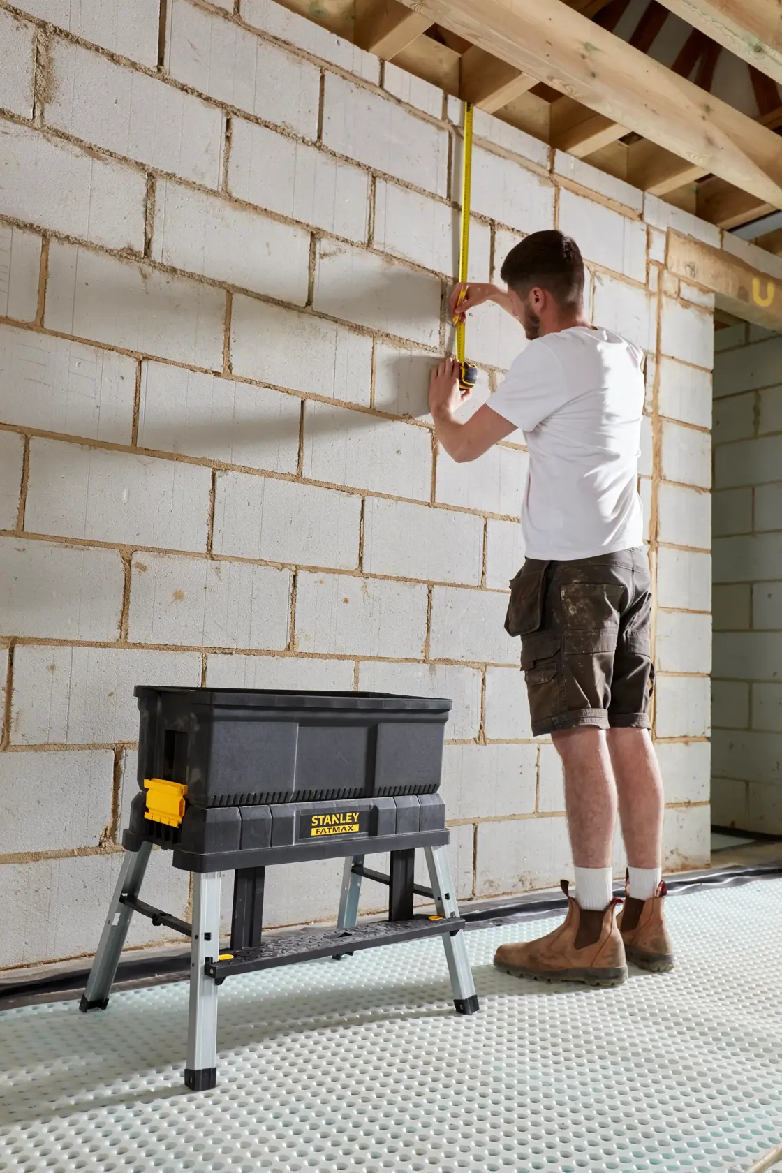 STANLEY FMST81083-1 black foldable sawhorse tool box on site, construction worker measuring wall.