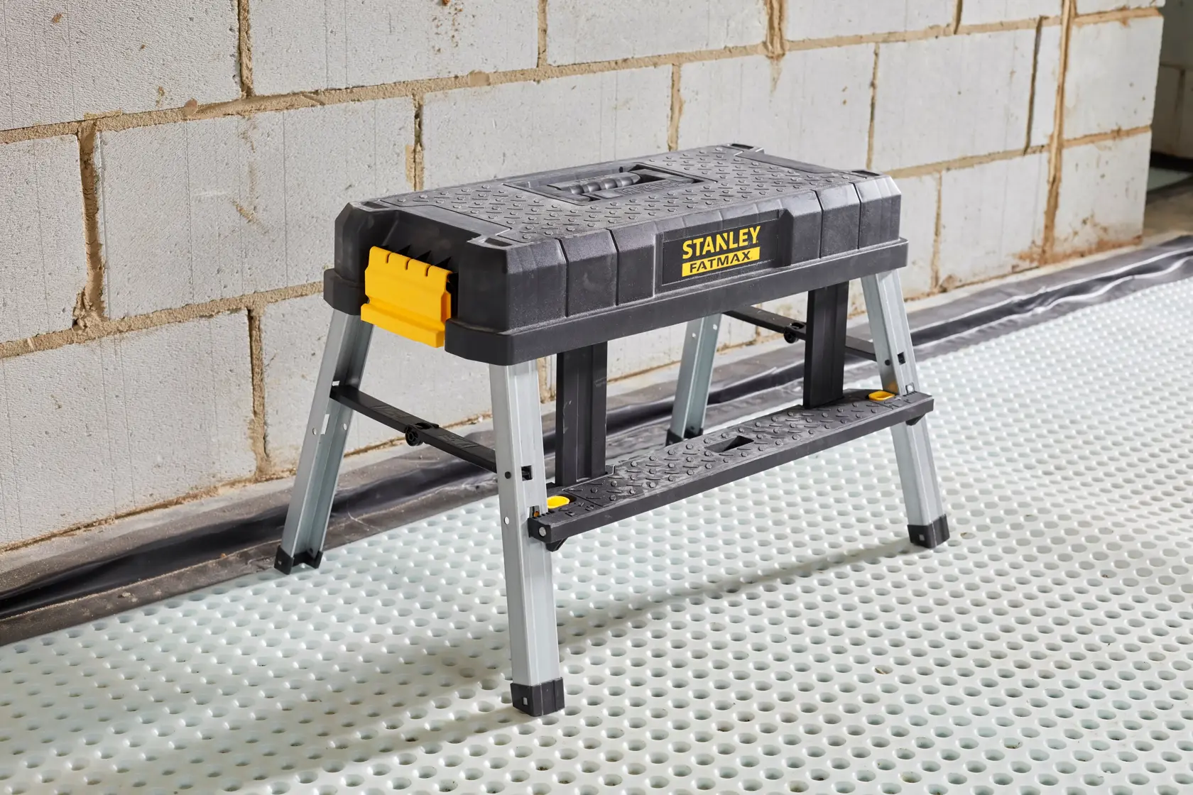 STANLEY FMST81083-1 step stool with black and yellow plastic top and metal legs, side angle, indoors.