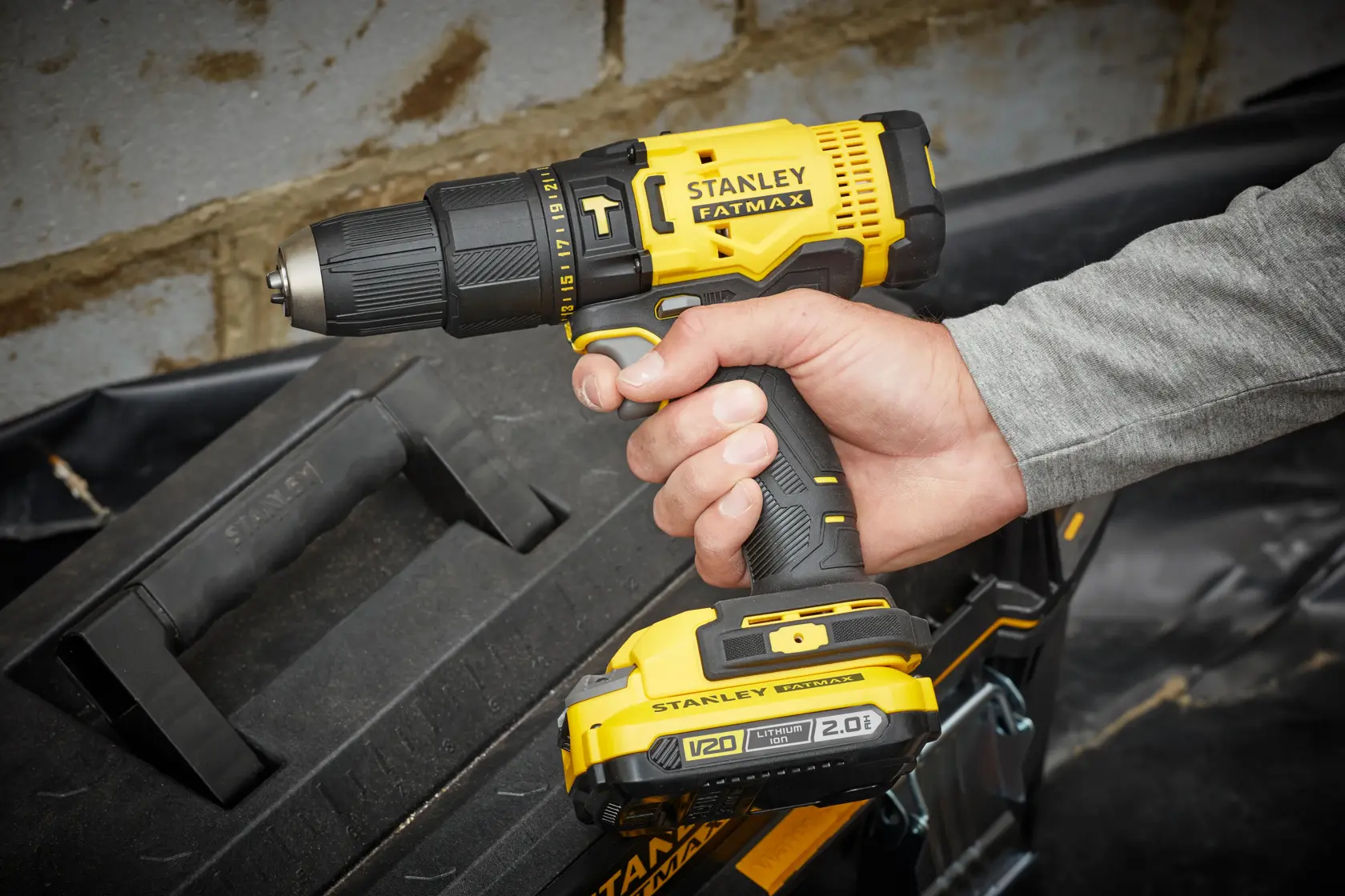 Photo of STANLEY SFMCD711D11 cordless drill being held, yellow and black, with FATMAX branding, near toolbox.
