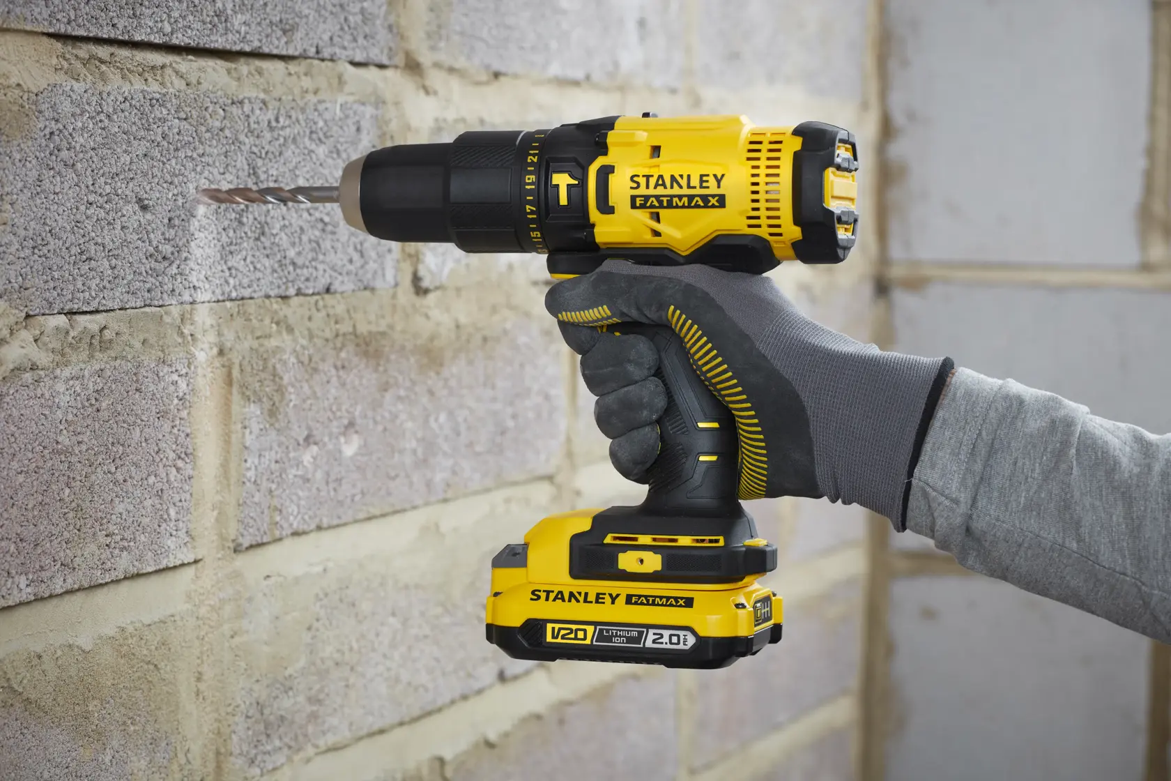 STANLEY SFMCD711D11 cordless drill, yellow and black, in use drilling brick wall.