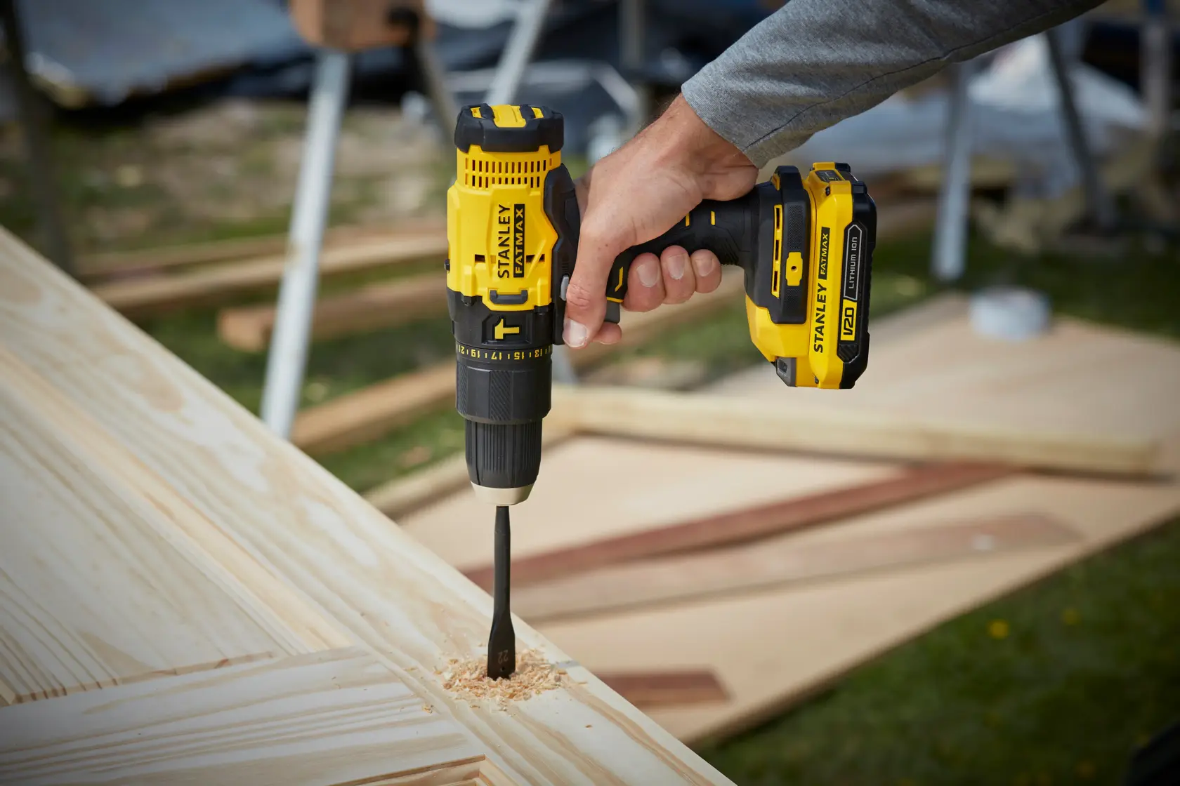 STANLEY SFMCD711D21 cordless drill driving bit into wood, product held in hand outdoors.