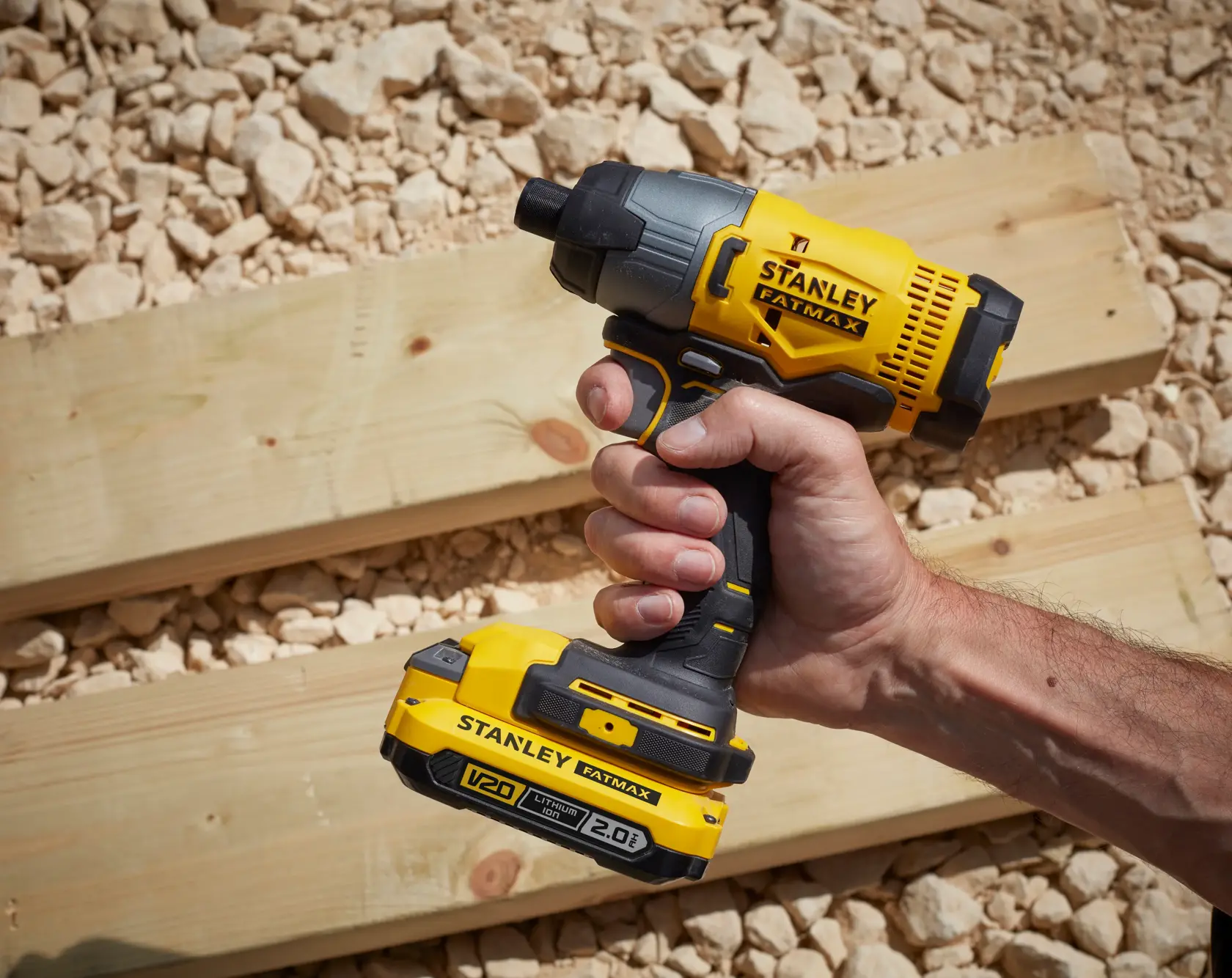 Photo of STANLEY SFMCF800D1K impact driver, yellow and black, held in hand on wood planks outdoors.