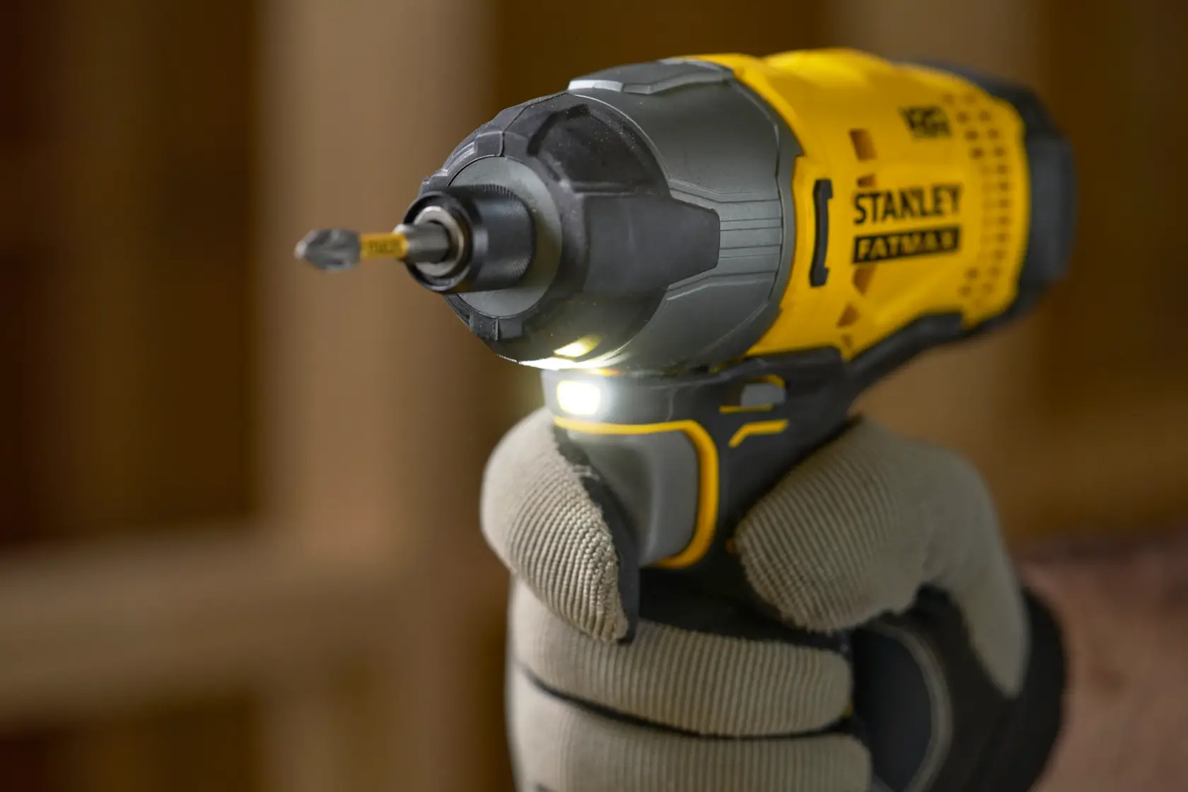Stanley yellow cordless impact driver held by a gloved hand, with LED light on and bit inserted.