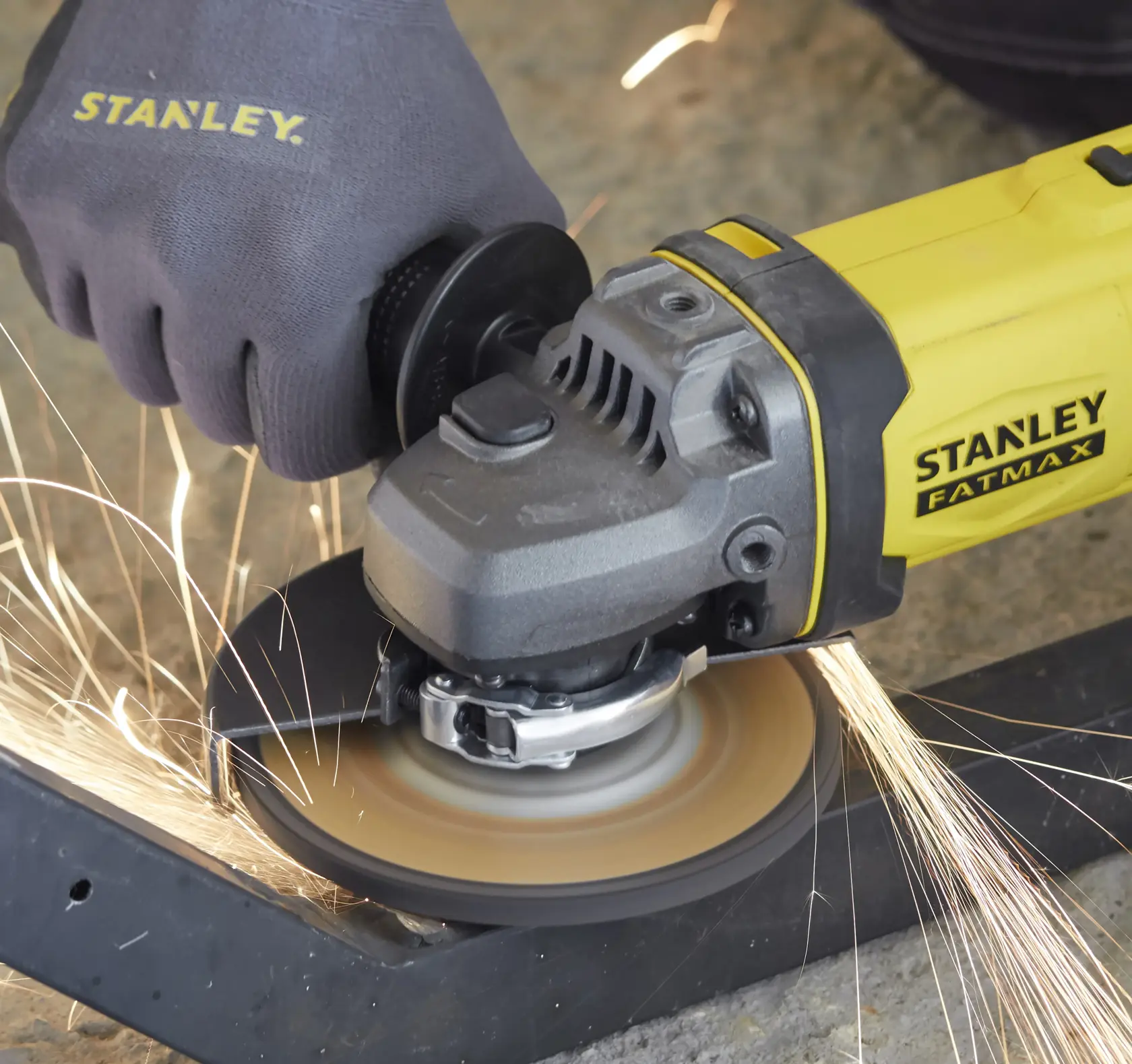 Stanley SFMCG400D1K angle grinder in use, yellow body, cutting metal with sparks, close-up.