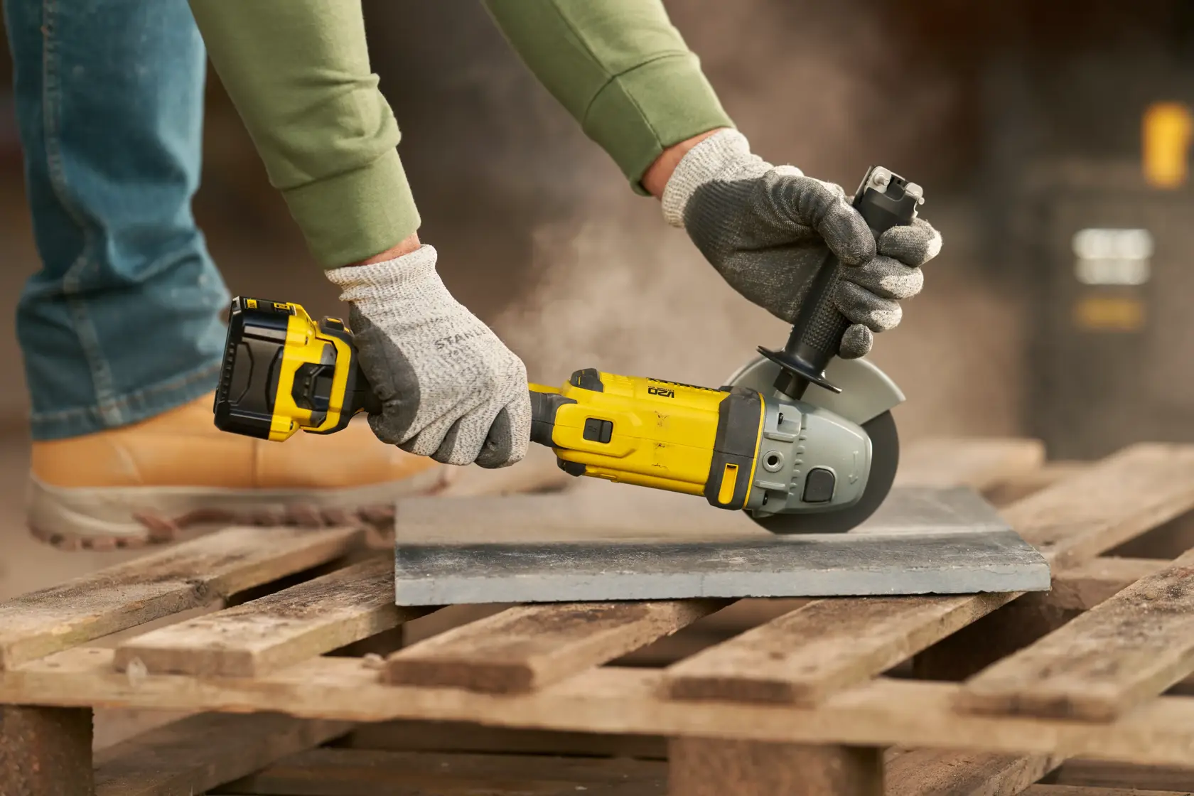 STANLEY SFMCG400M1K angle grinder in use cutting tile, yellow and black tool on wooden pallet outdoors.