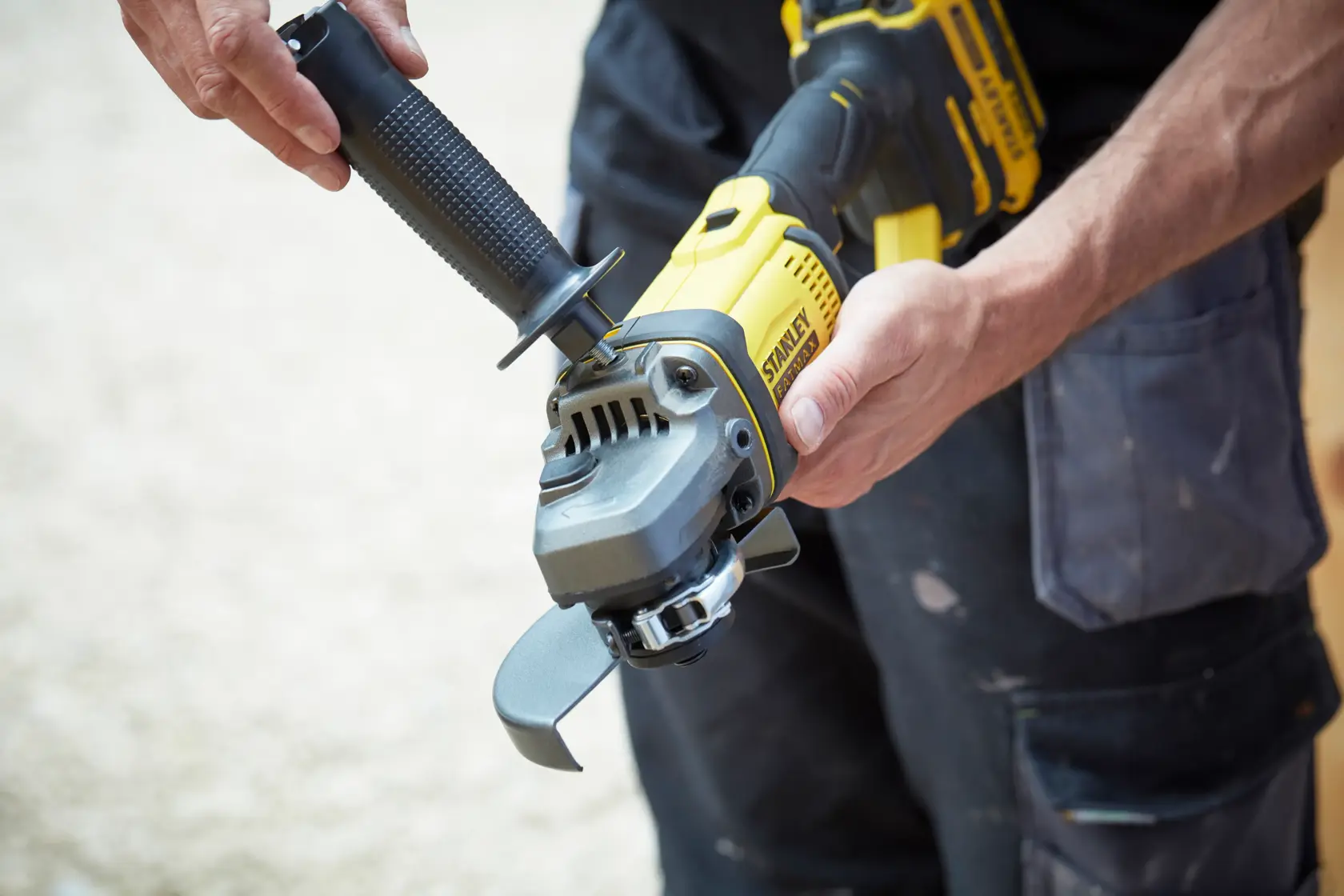 Photo of STANLEY SFMCG400M1K cordless angle grinder being held with black and yellow handle, side view.
