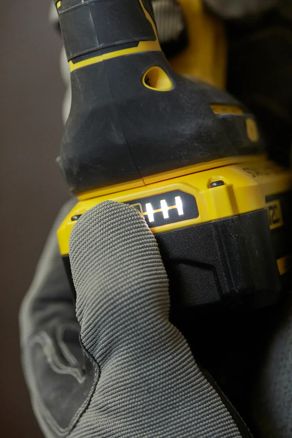 Photo of STANLEY SFMCH900M12 cordless drill battery indicator close-up, gloved hand pressing indicator button.