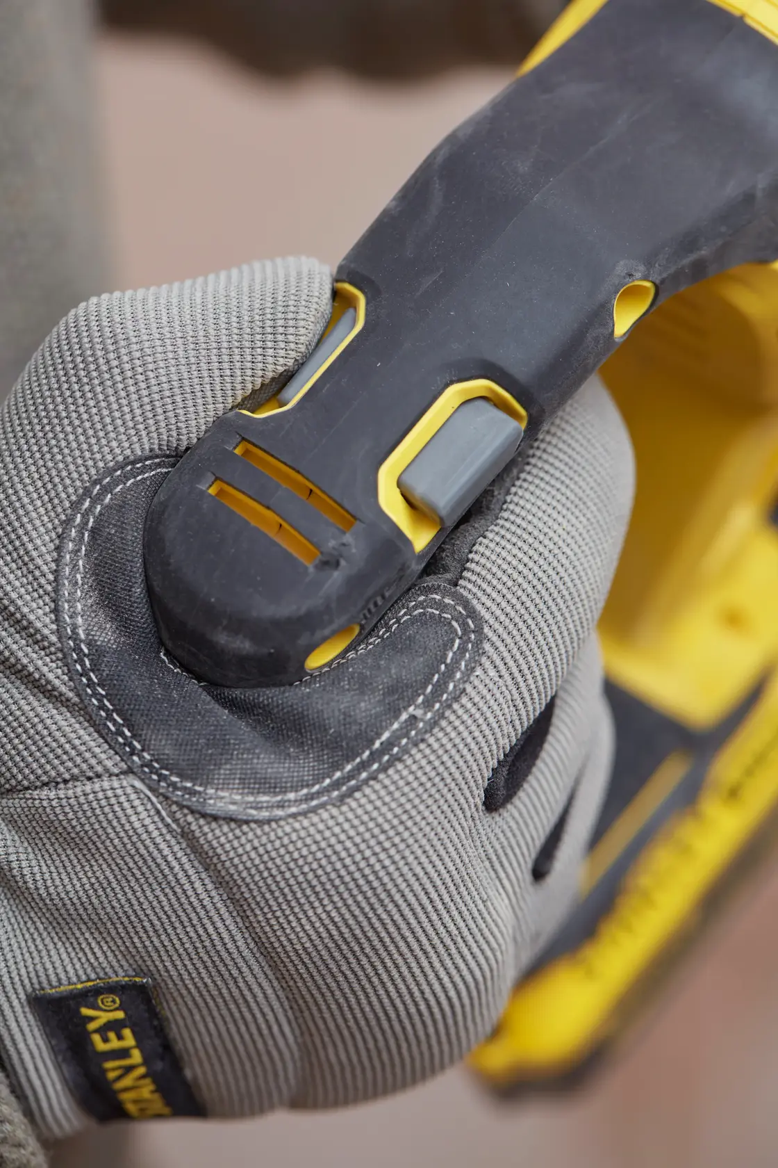 Photo of a gloved hand gripping the handle of a STANLEY SFMCH900M12 power tool, showing the trigger area.