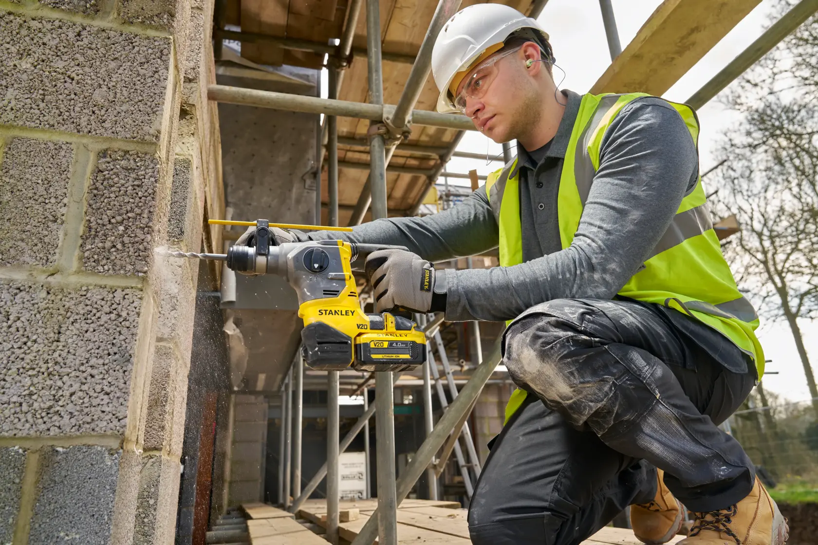 Worker using STANLEY SFMCH910B cordless rotary hammer drill on concrete wall at construction site.
