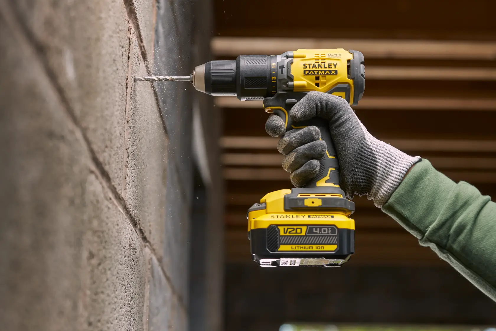 Stanley SFMCK461M2S cordless drill in use on a concrete wall, close-up side view, worker wearing gloves.