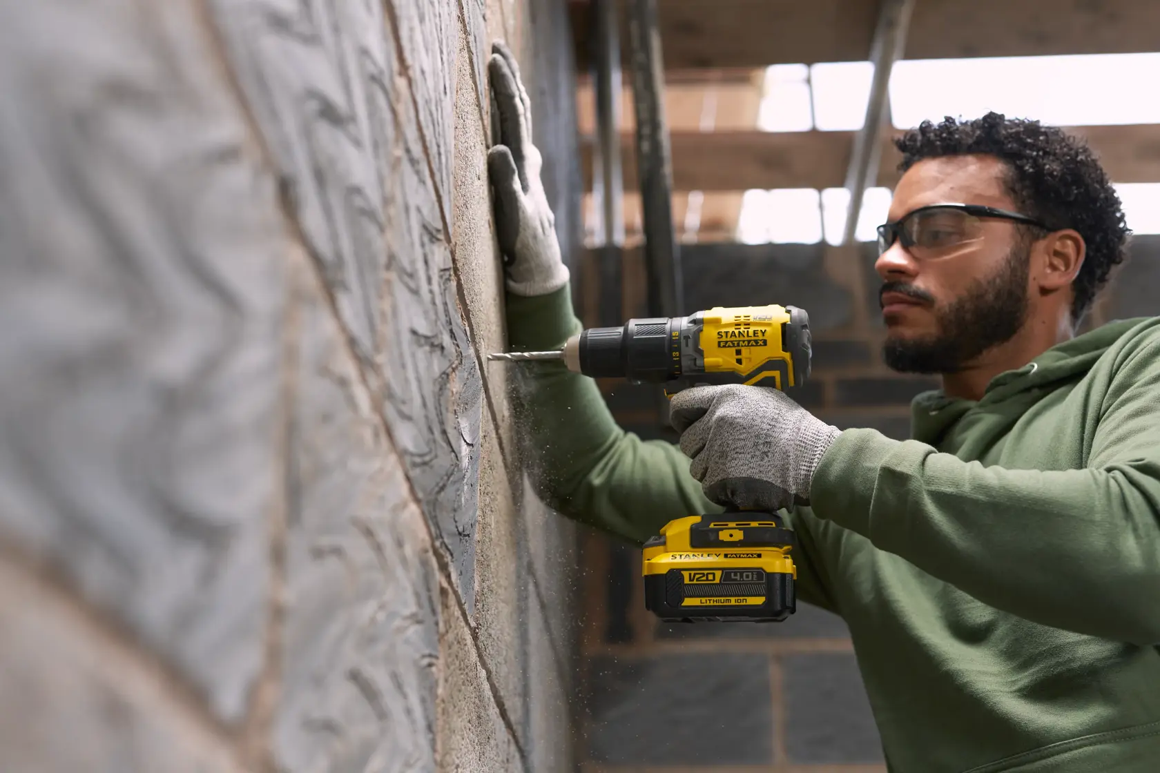 Photo of STANLEY SFMCK461M2S cordless drill in use, drilling into a concrete wall, held by person wearing gloves.