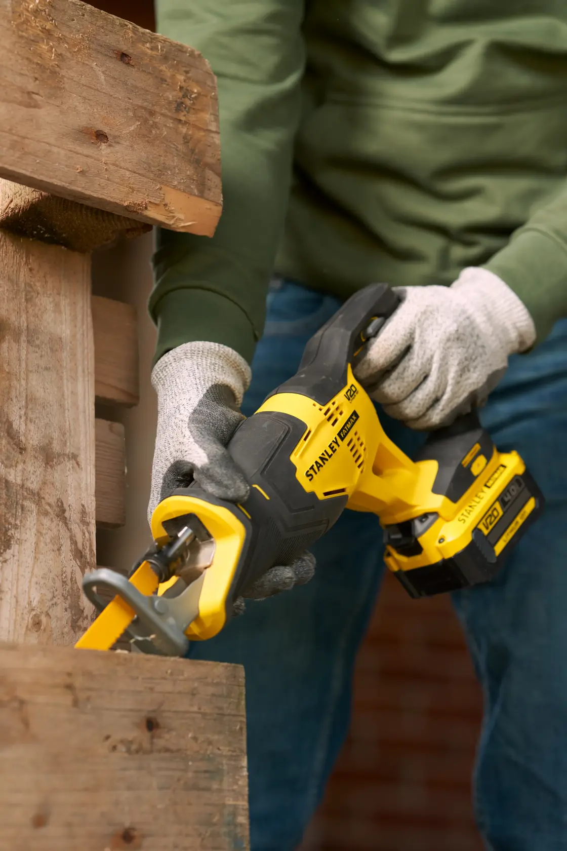STANLEY SFMCS300M1K cordless reciprocating saw in use cutting wooden plank, close-up with worker hands.
