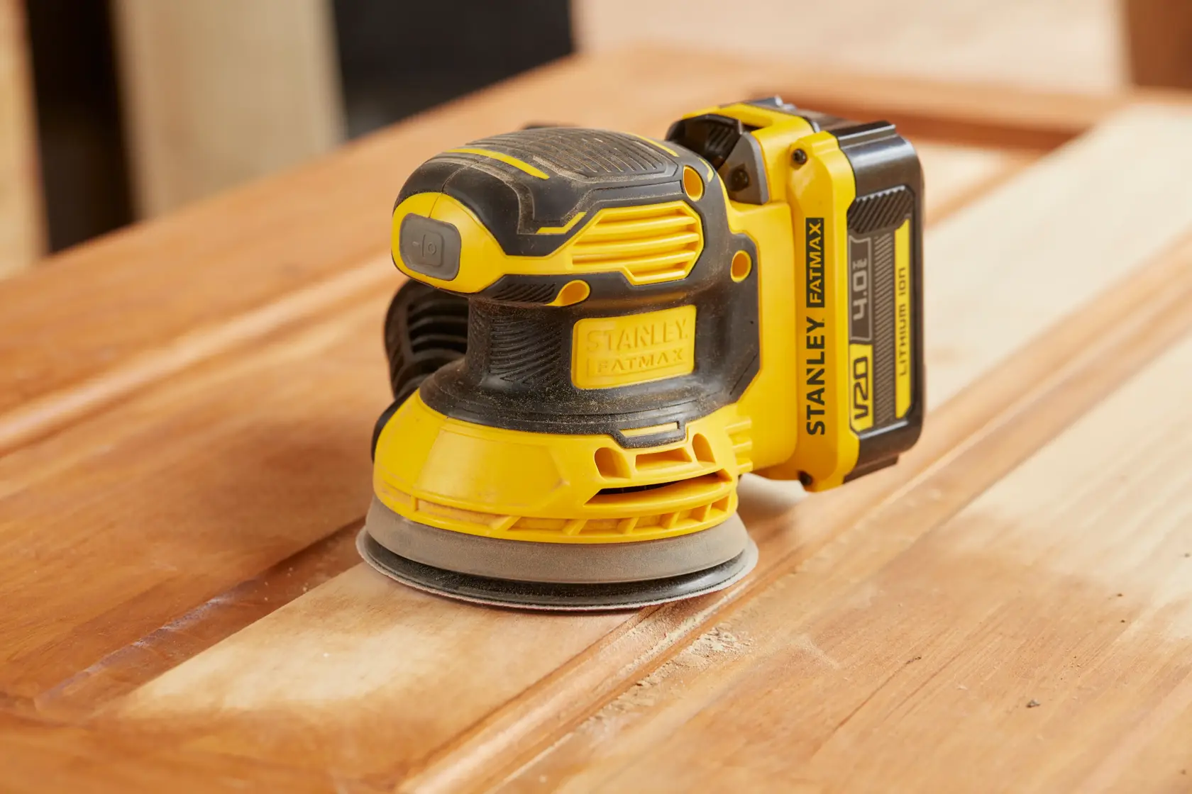 STANLEY SFMCW220M1S cordless random orbital sander in yellow and black, sanding wooden surface, close-up.
