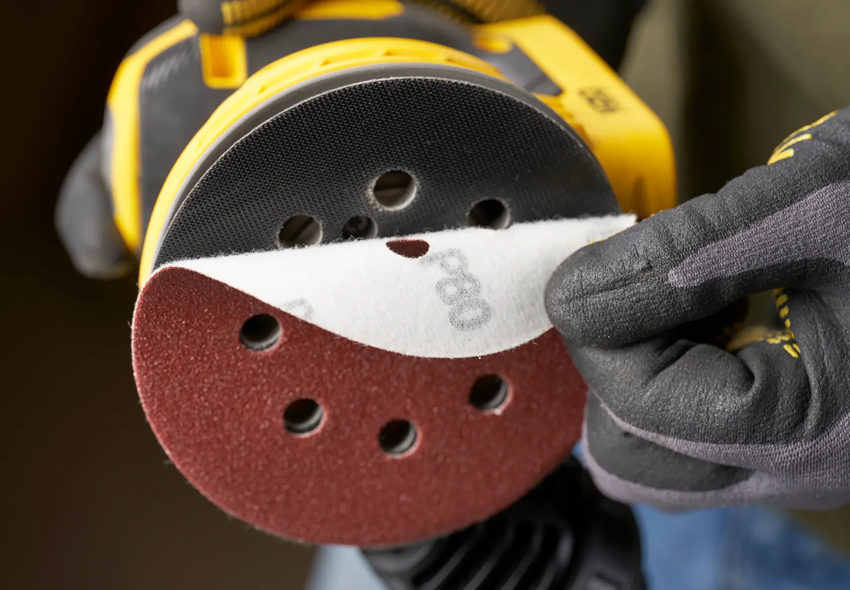 STANLEY STA32392 sanding disc being attached to a yellow power sander, close-up angle, product photography.