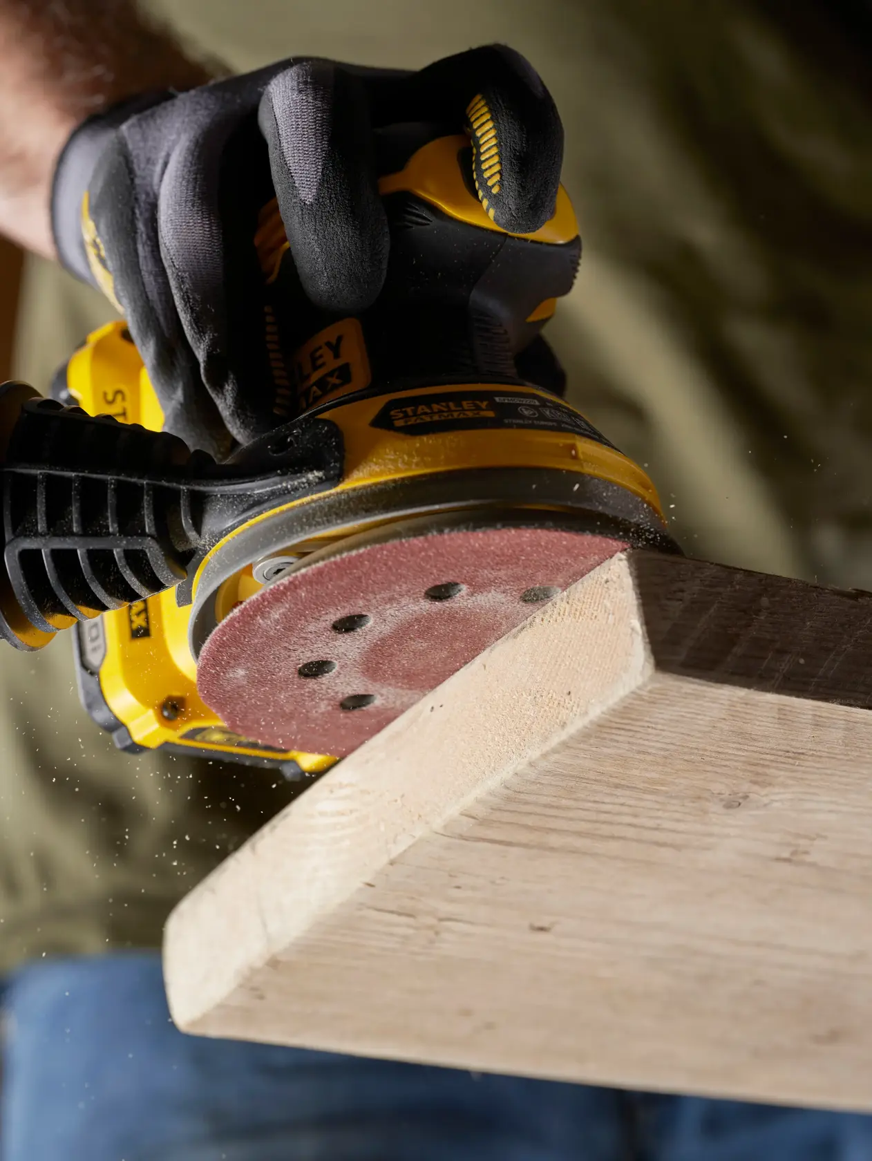 STANLEY STA32392 sander in use on wood, close-up showing gloved hand and sanding disc.