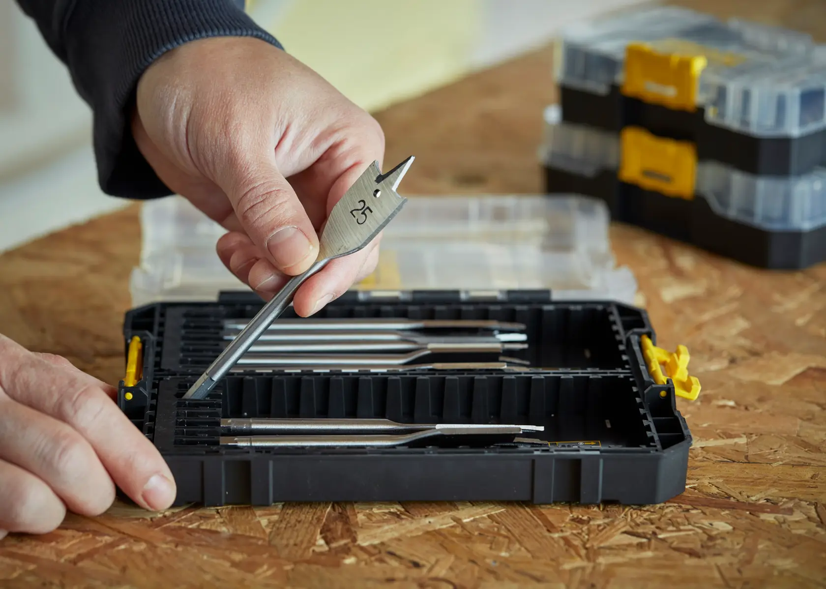 STANLEY STA88556 drill bit set in black case, hand holding flat wood drill bit, case open on wood surface.