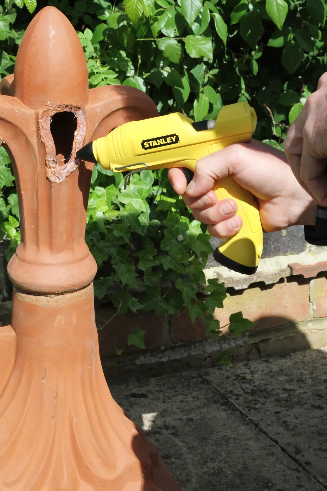 STANLEY STHT0-70416 yellow glue gun being used on broken terracotta garden ornament outdoors.