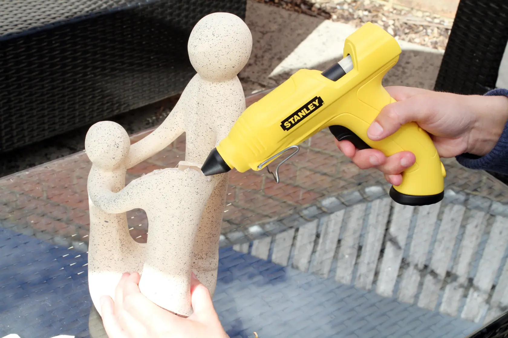 STANLEY STHT0-70416 yellow glue gun in use, bonding a beige sculpture on a glass table.