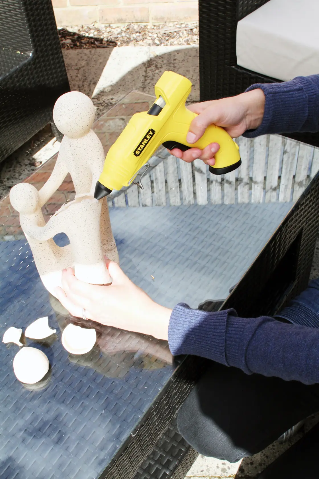 STANLEY STHT0-70416 glue gun repairing ceramic statue, outdoor setting, hand holding yellow tool.