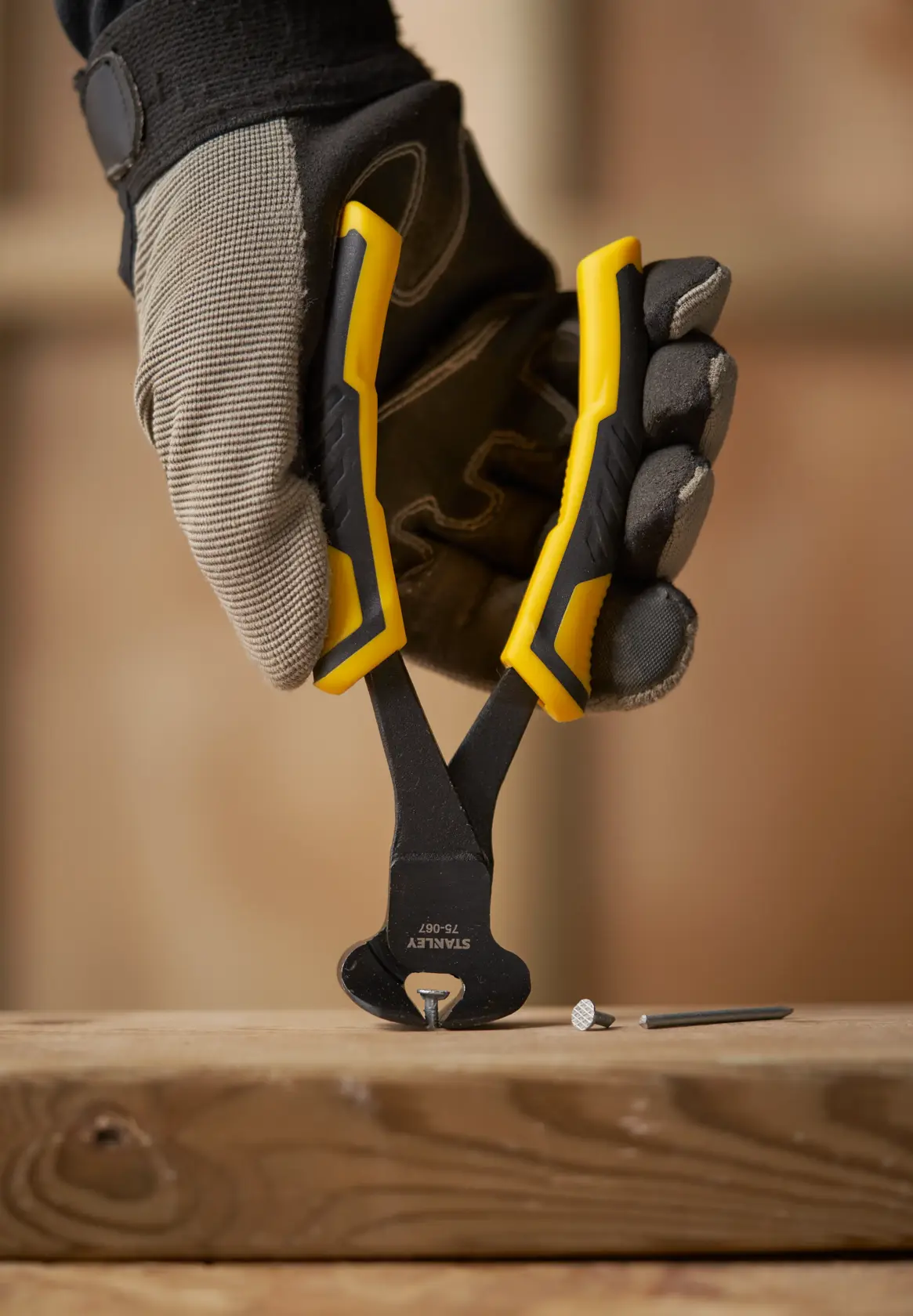 Photo of STANLEY STHT0-75067 yellow-handled end cutting pliers held by gloved hand, removing nail from wood.