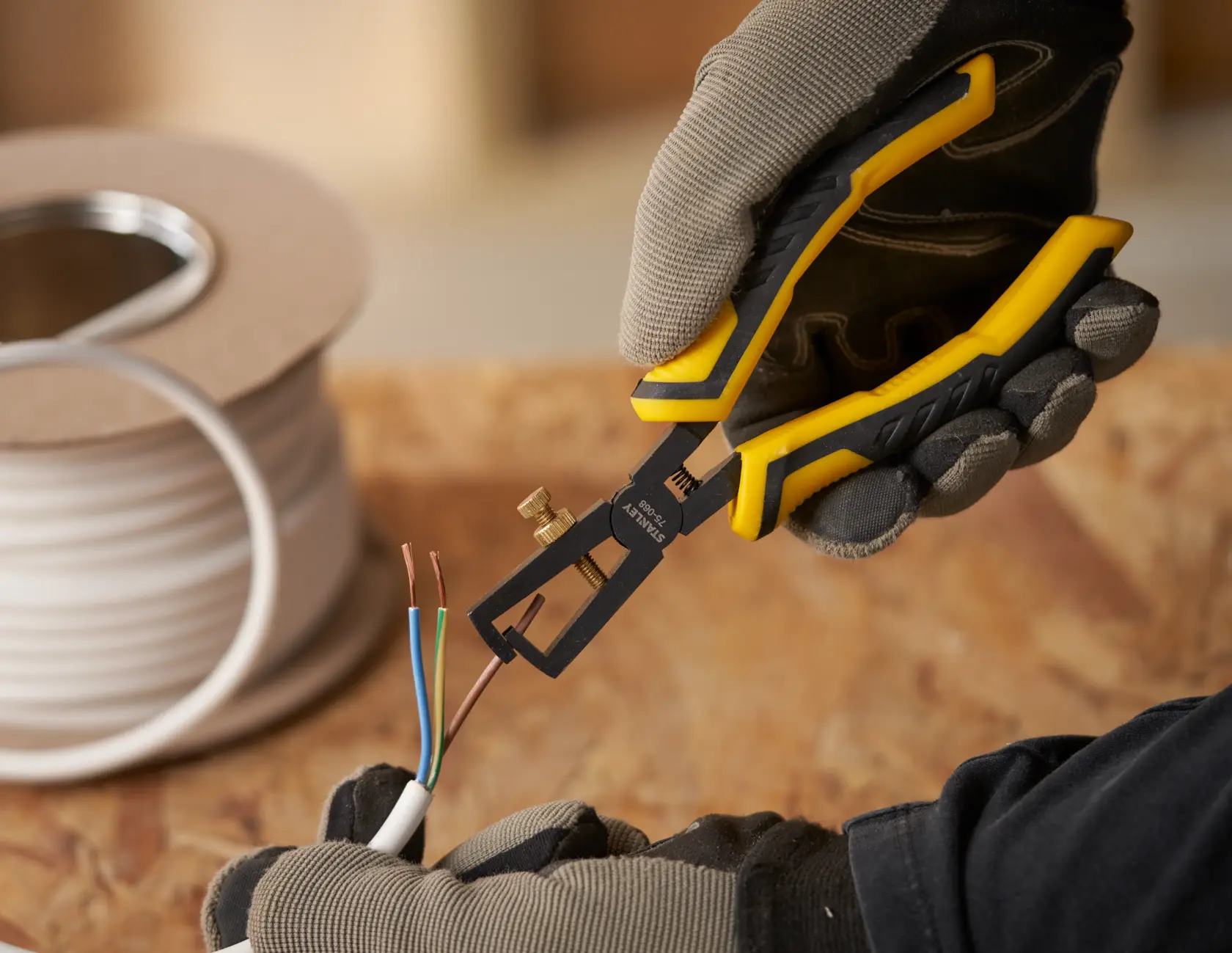 STANLEY STHT0-75068 wire stripper held by gloved hand, stripping colored wires on wooden surface.