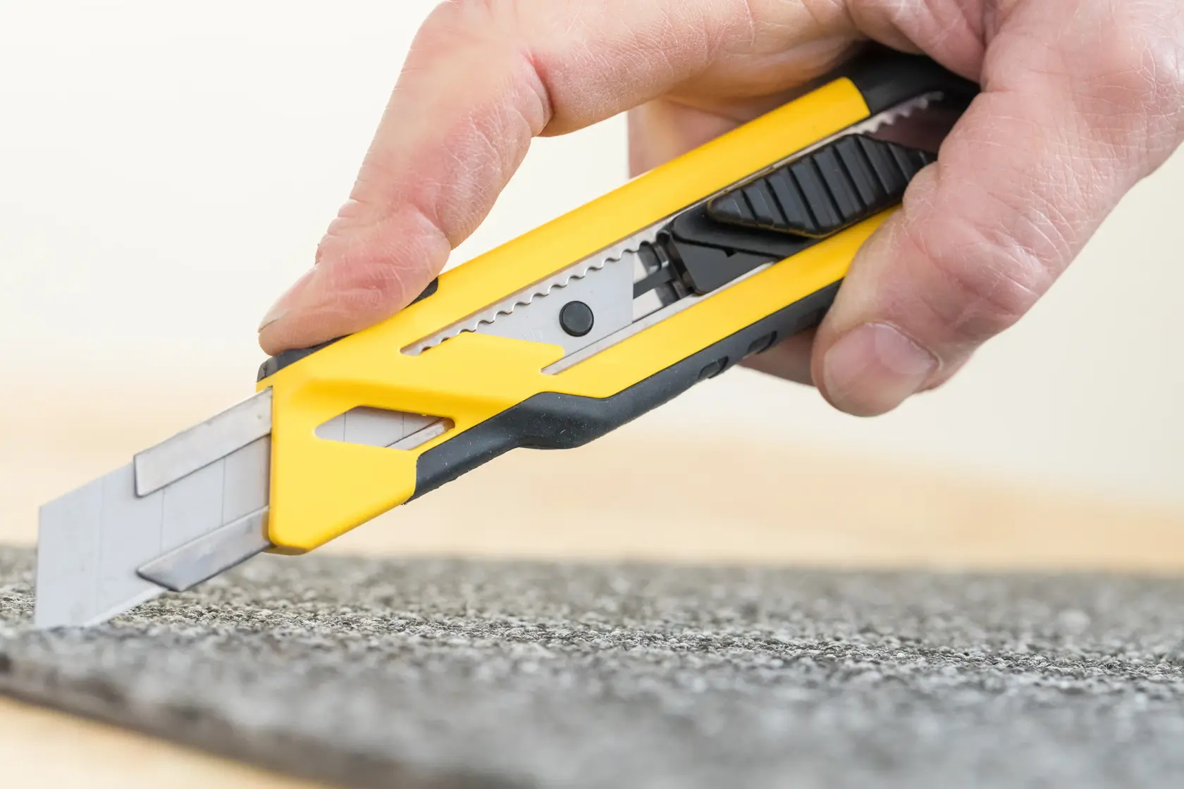 STANLEY STHT10266-0 utility knife close-up cutting carpet, yellow and black handle.