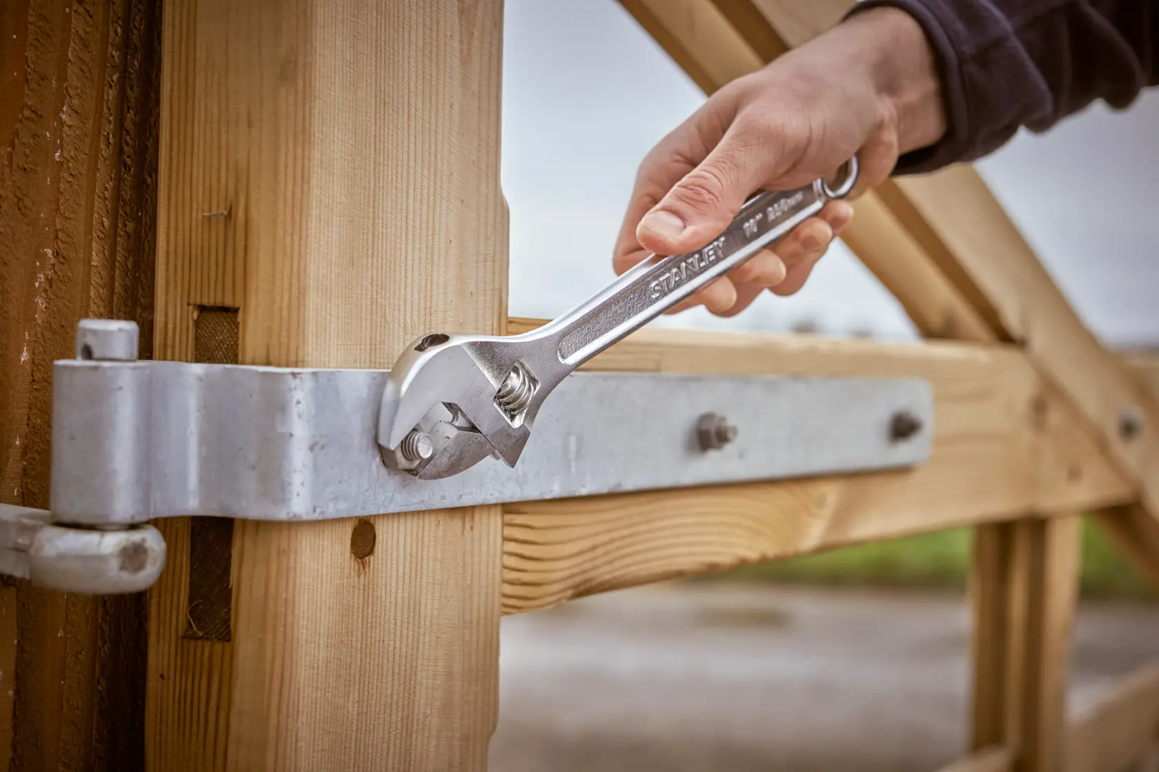 STANLEY STHT13122-0 adjustable wrench tightening a metal bolt on a wooden gate in outdoor setting.