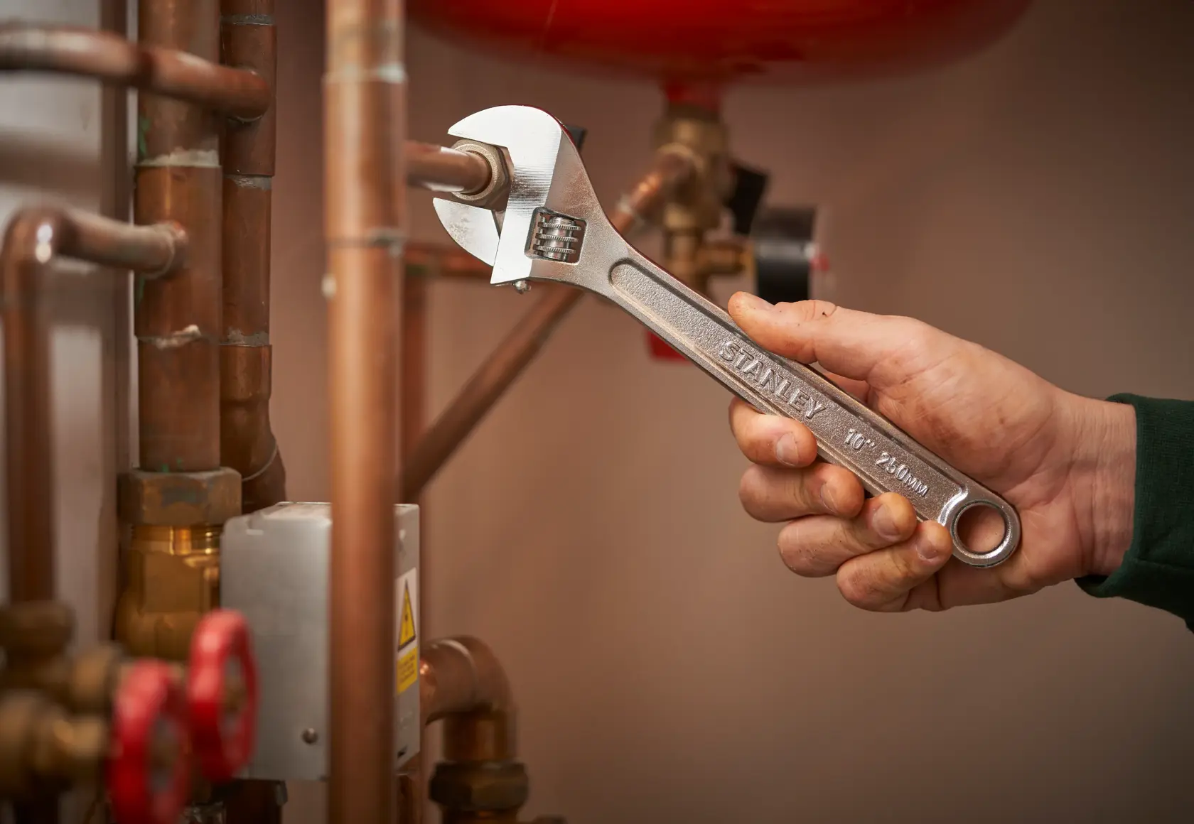 STANLEY STHT13122-0 adjustable wrench used on copper pipes in plumbing setting.