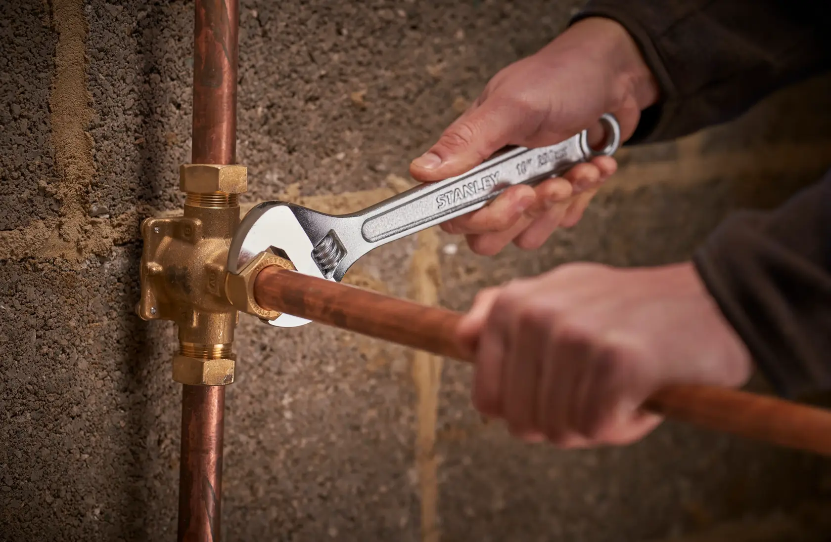 Photo of STANLEY STHT13122-0 adjustable wrench being used on copper plumbing pipe against masonry wall.