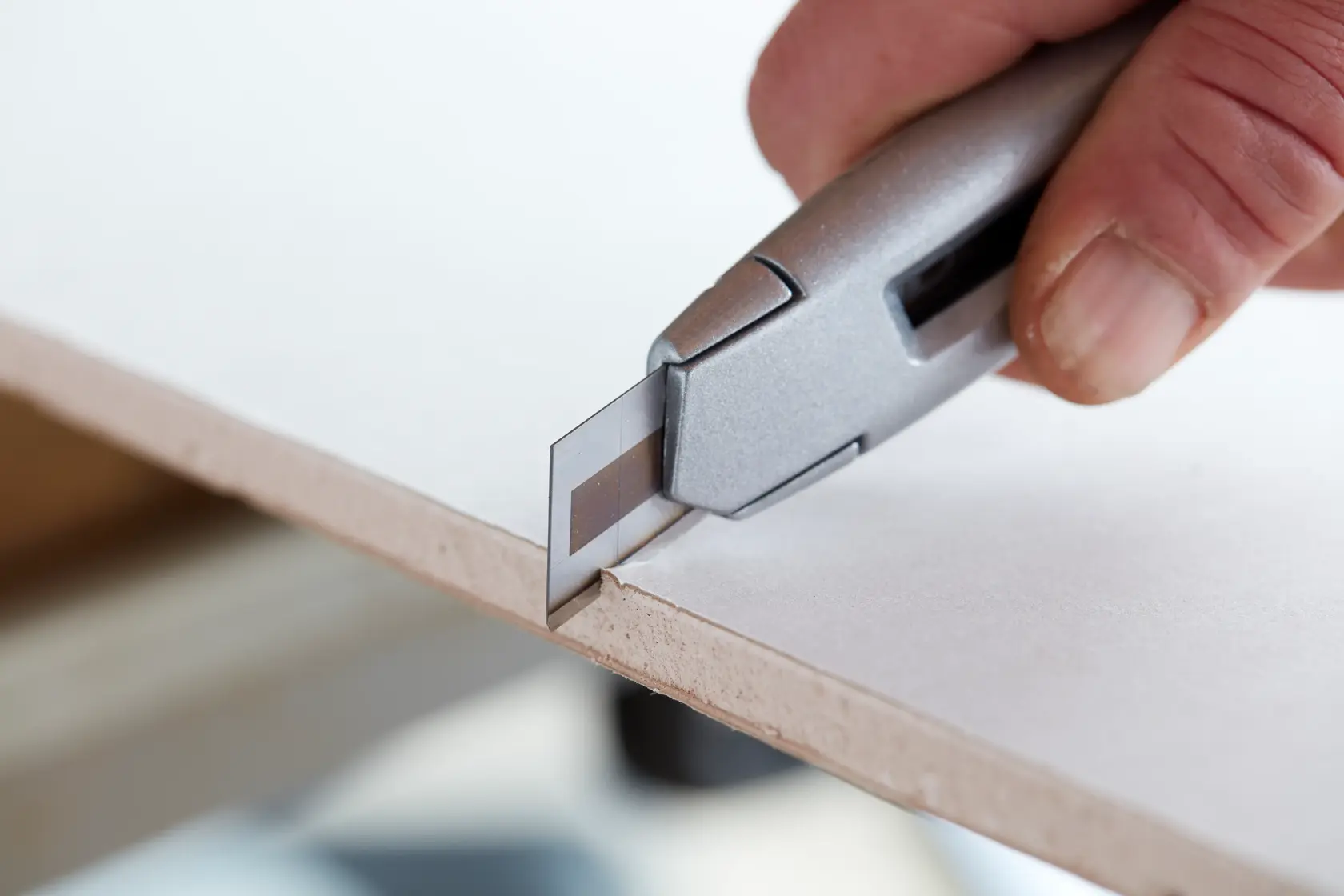 STANLEY STHT2-11818 utility knife cutting drywall close-up, silver handle, photography.