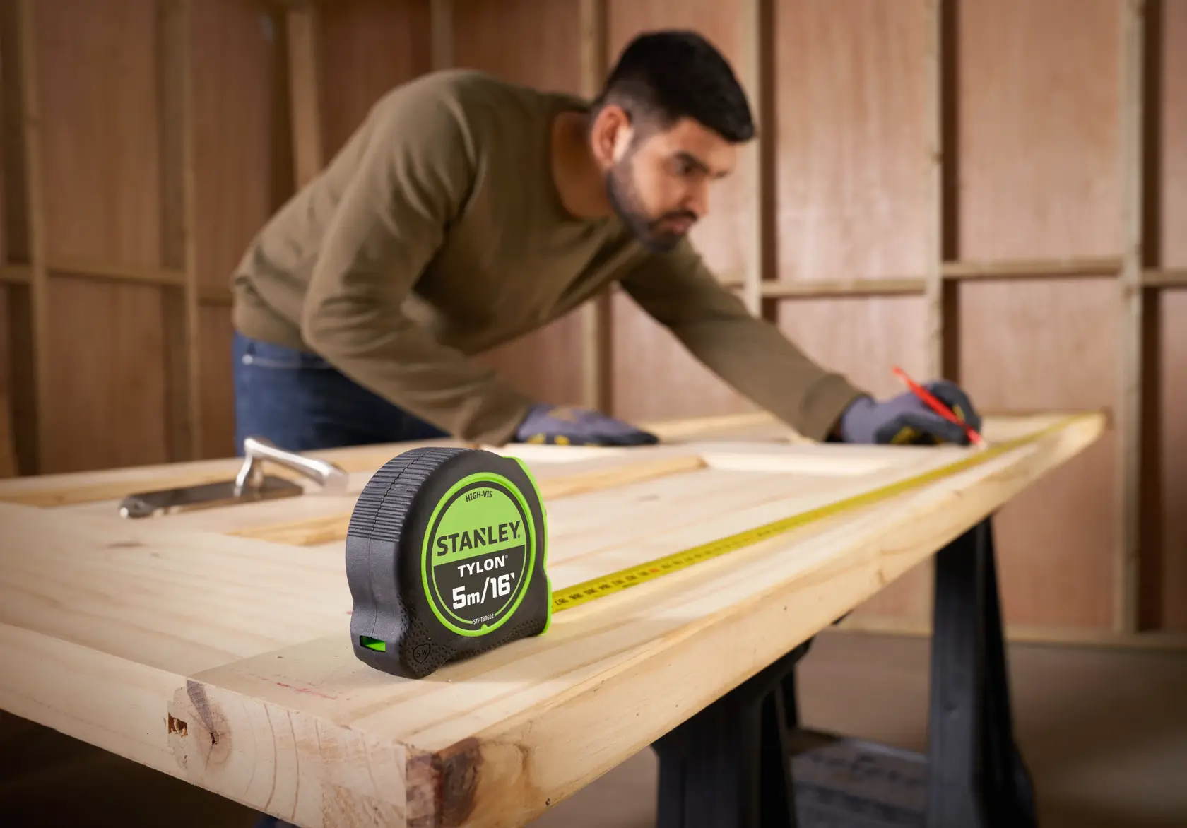 STANLEY STHT30602-1 tape measure on wooden table, person measuring wood, workshop setting.